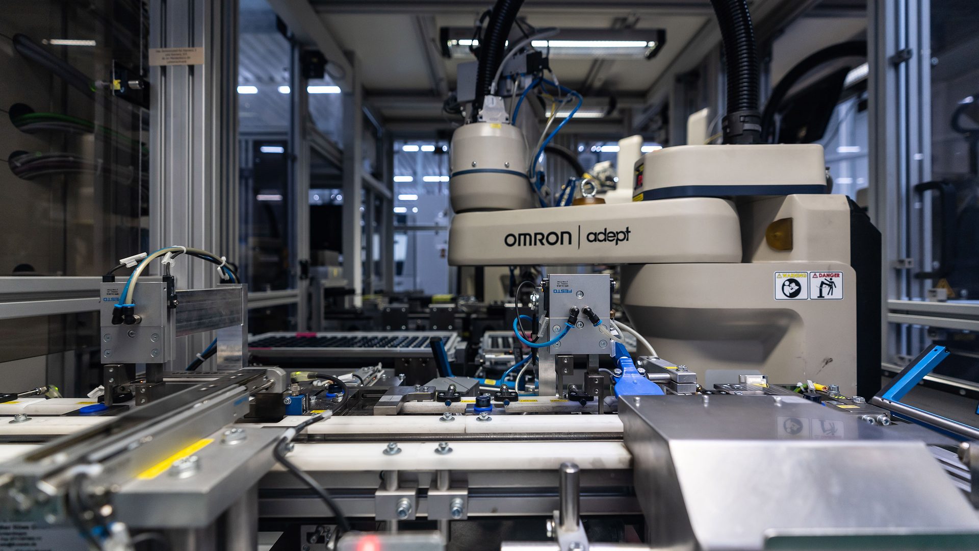 Omron Adept industrial robot on an automated assembly line with precision machinery.
