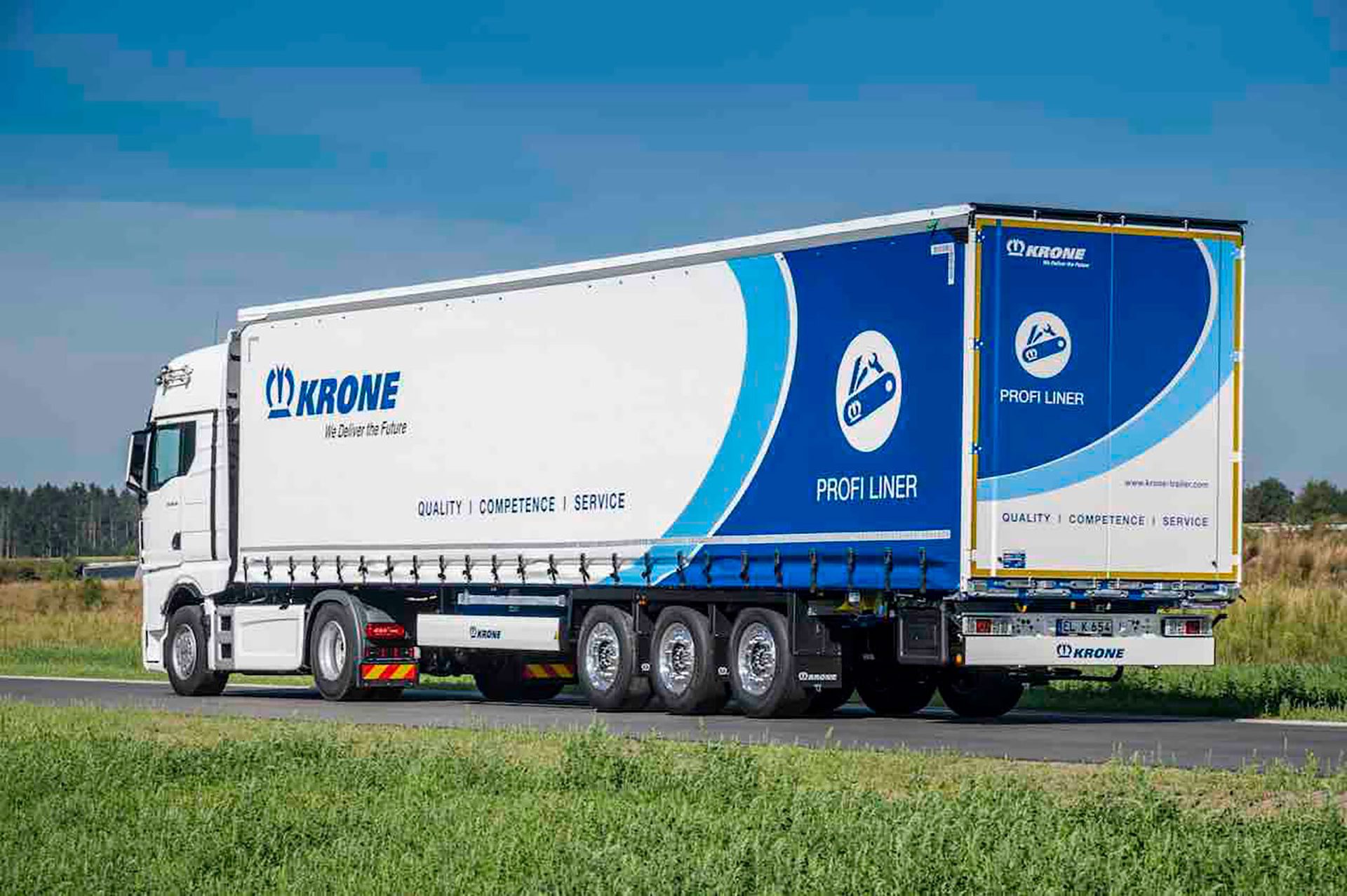 White truck hauling a blue and white 'KRONE Profi Liner' trailer on a road.
