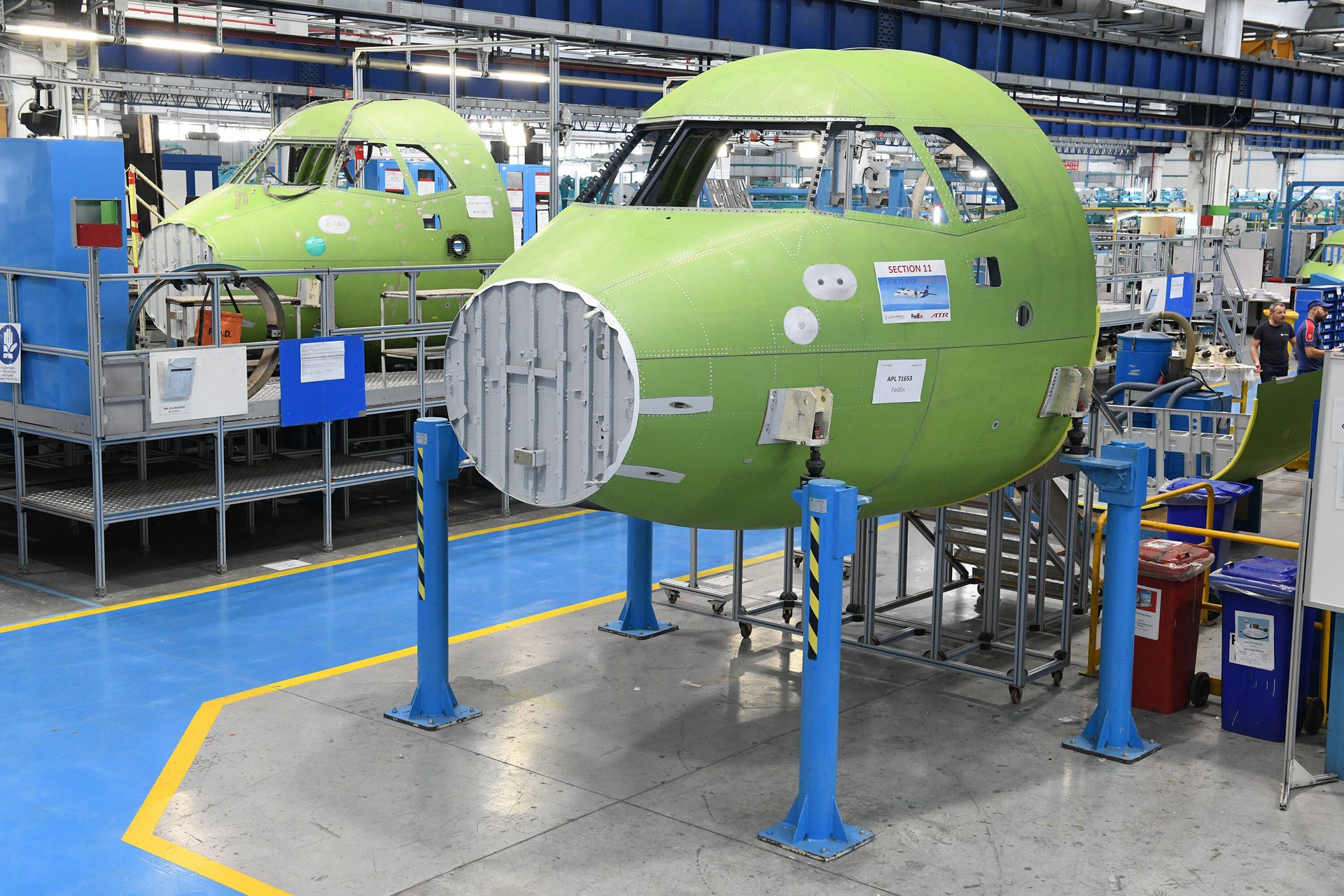 Two light green FedEx aircraft cockpit sections under assembly in a factory.