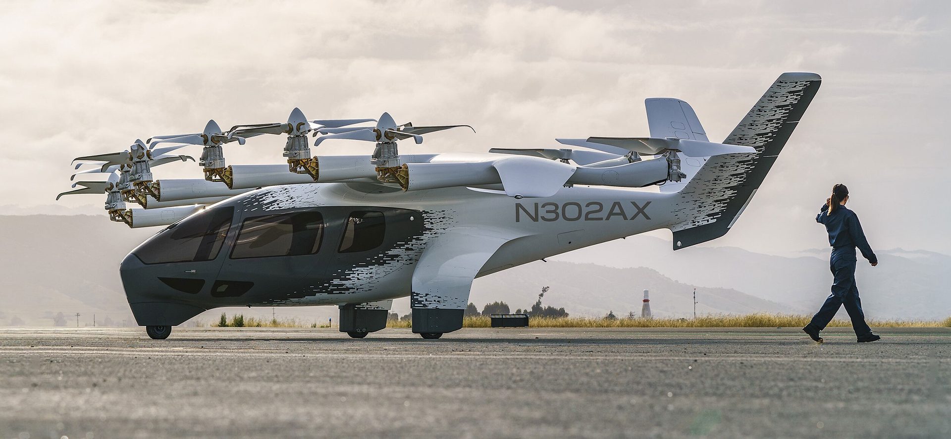 An eVTOL aircraft with multiple propellers on a tarmac, with a person walking away.