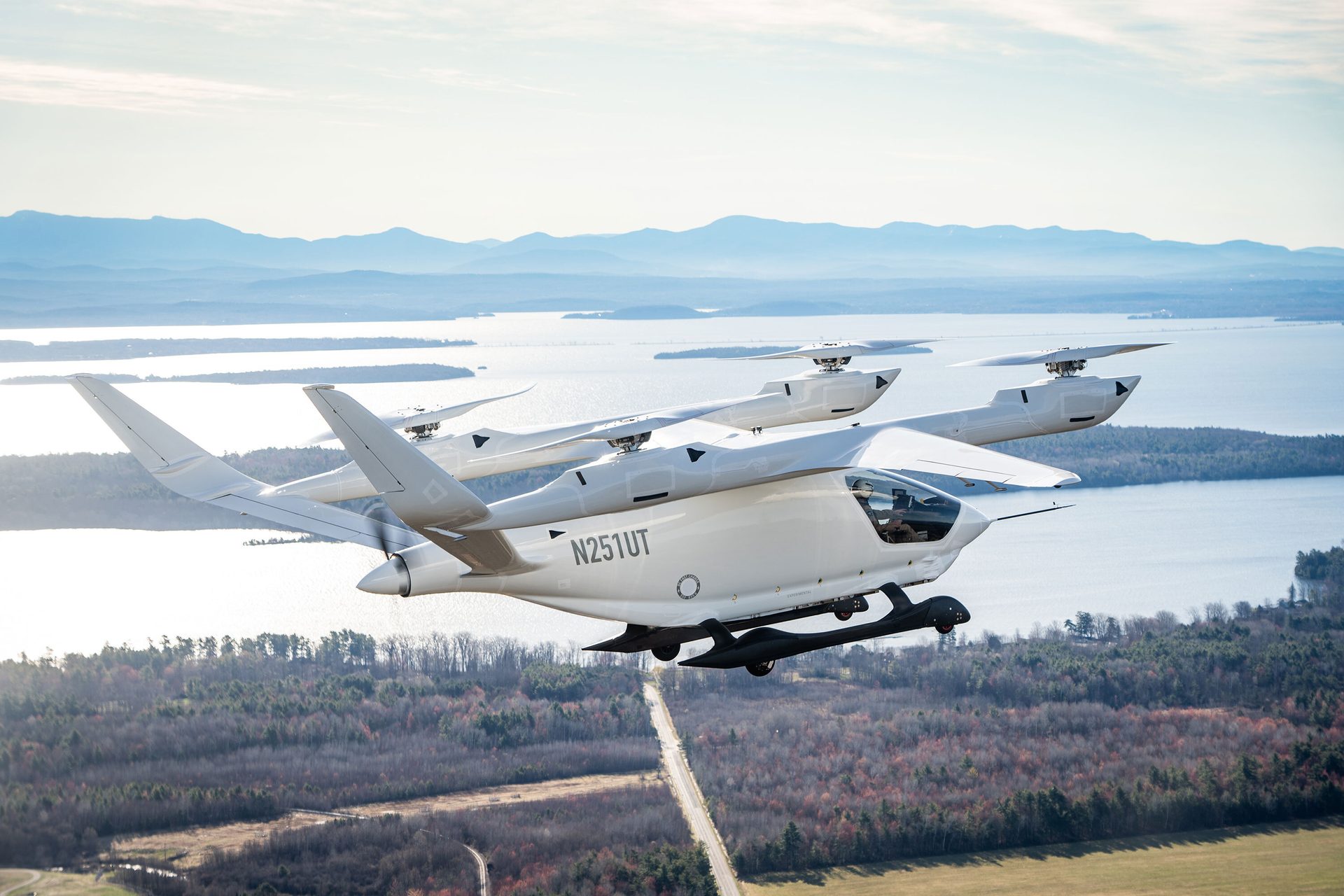 White multi-rotor aircraft flying over lakes and mountains on a clear day.