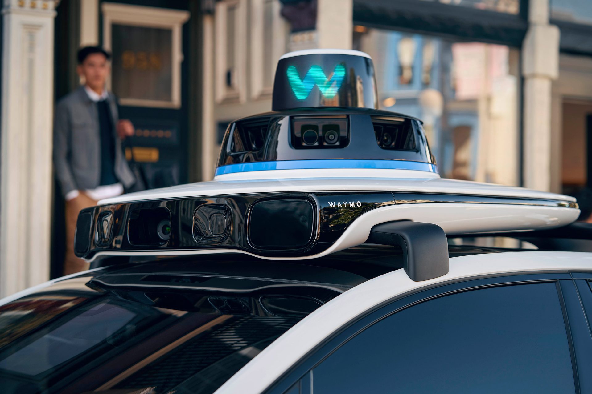 Waymo self-driving car's sensor dome with a blurred person in the background.