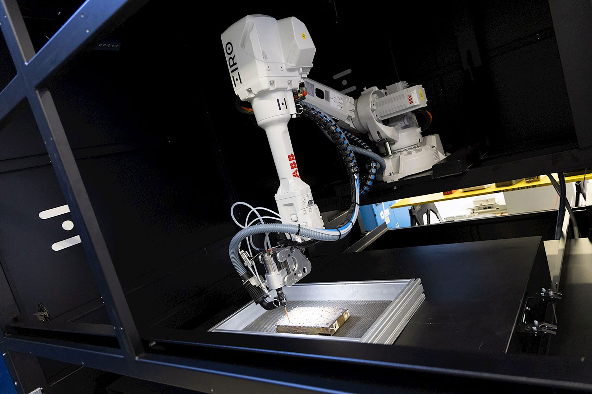 White ABB robotic arm performing additive manufacturing inside a dark chamber.