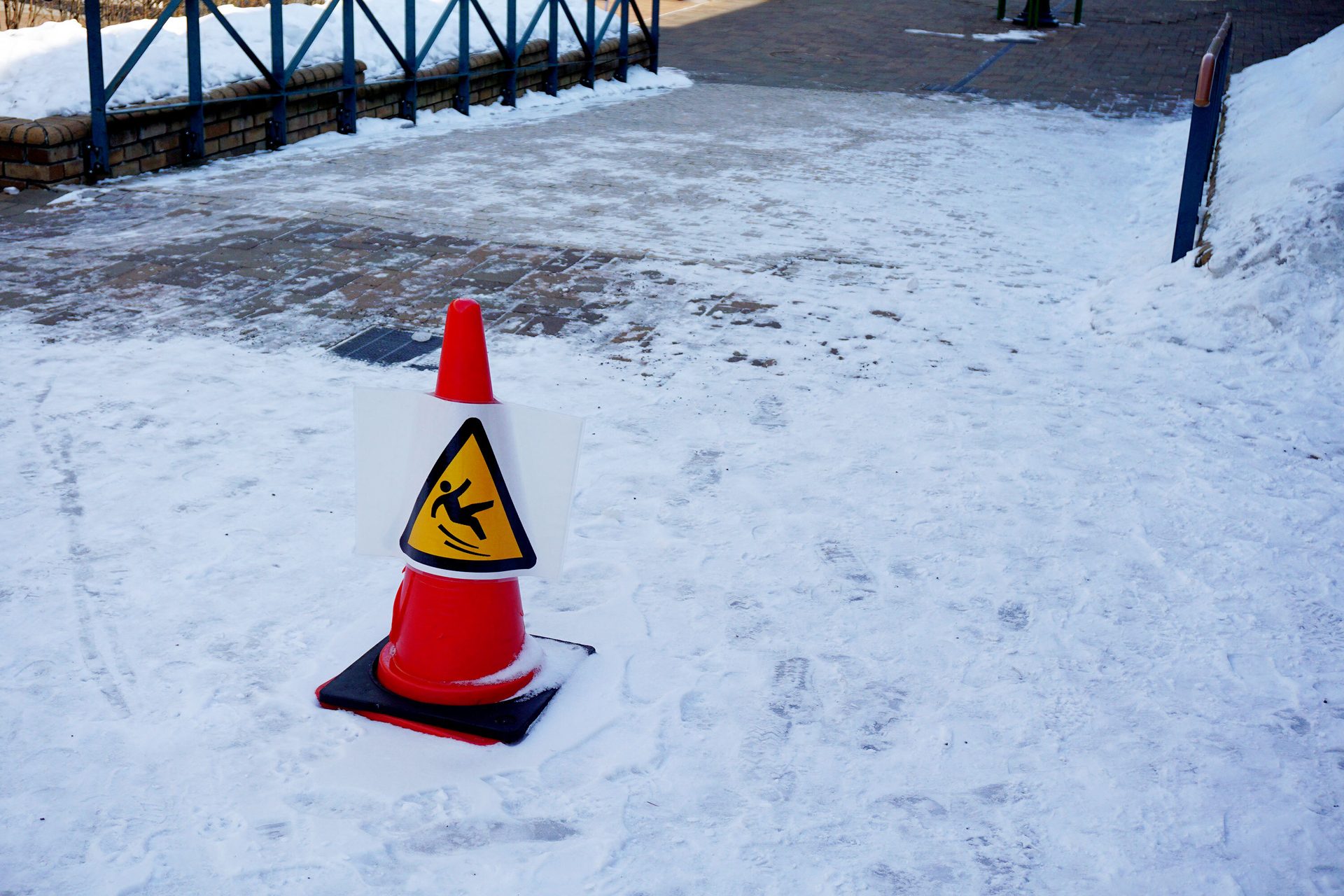 Red cone with a "slippery surface" sign on a snow-covered path.