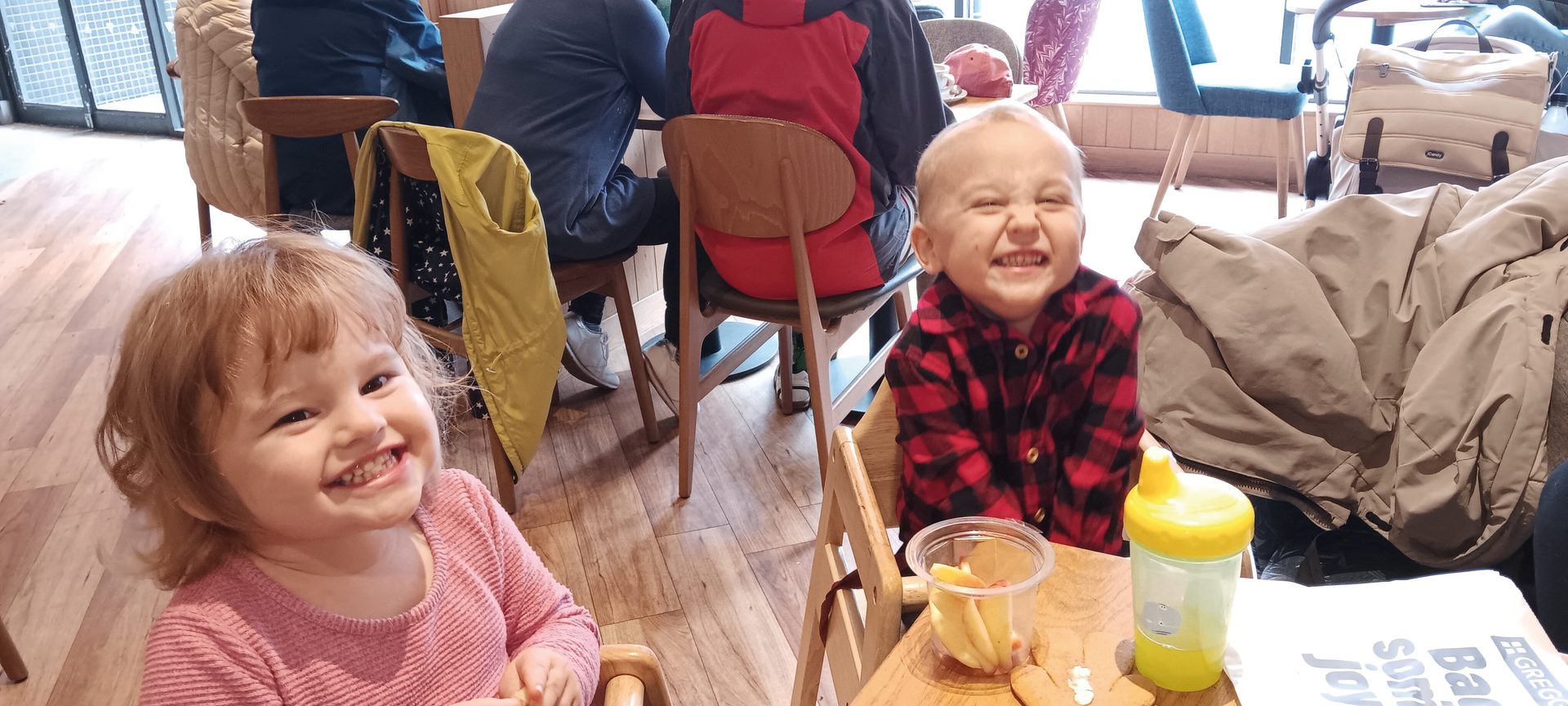 Two cheerful young children, a girl and a boy, smiling and making funny faces in a cafe.