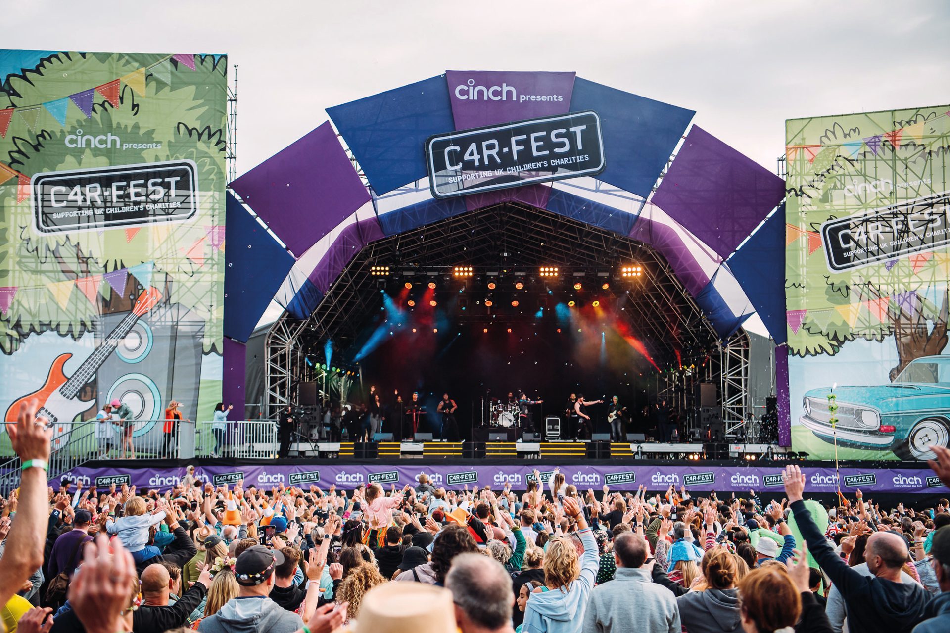 A live band performs on a large stage under Car-Fest banners to an enthusiastic crowd with hands raised.