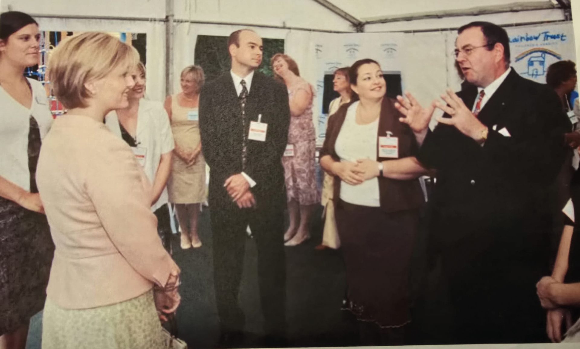 A group of people, including two men in suits and two women, engaging in conversation at an indoor event.