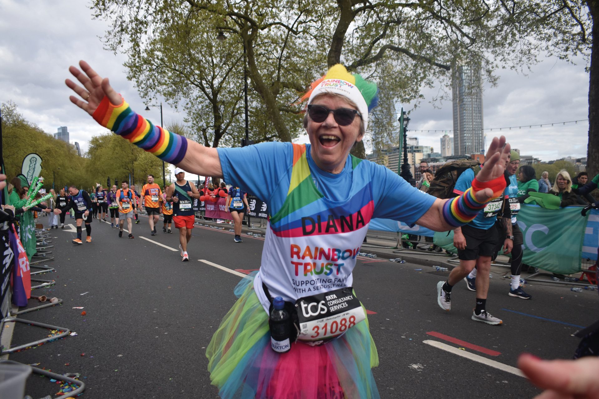 Cheerful marathon runner in rainbow attire, arms outstretched, celebrating during a race.