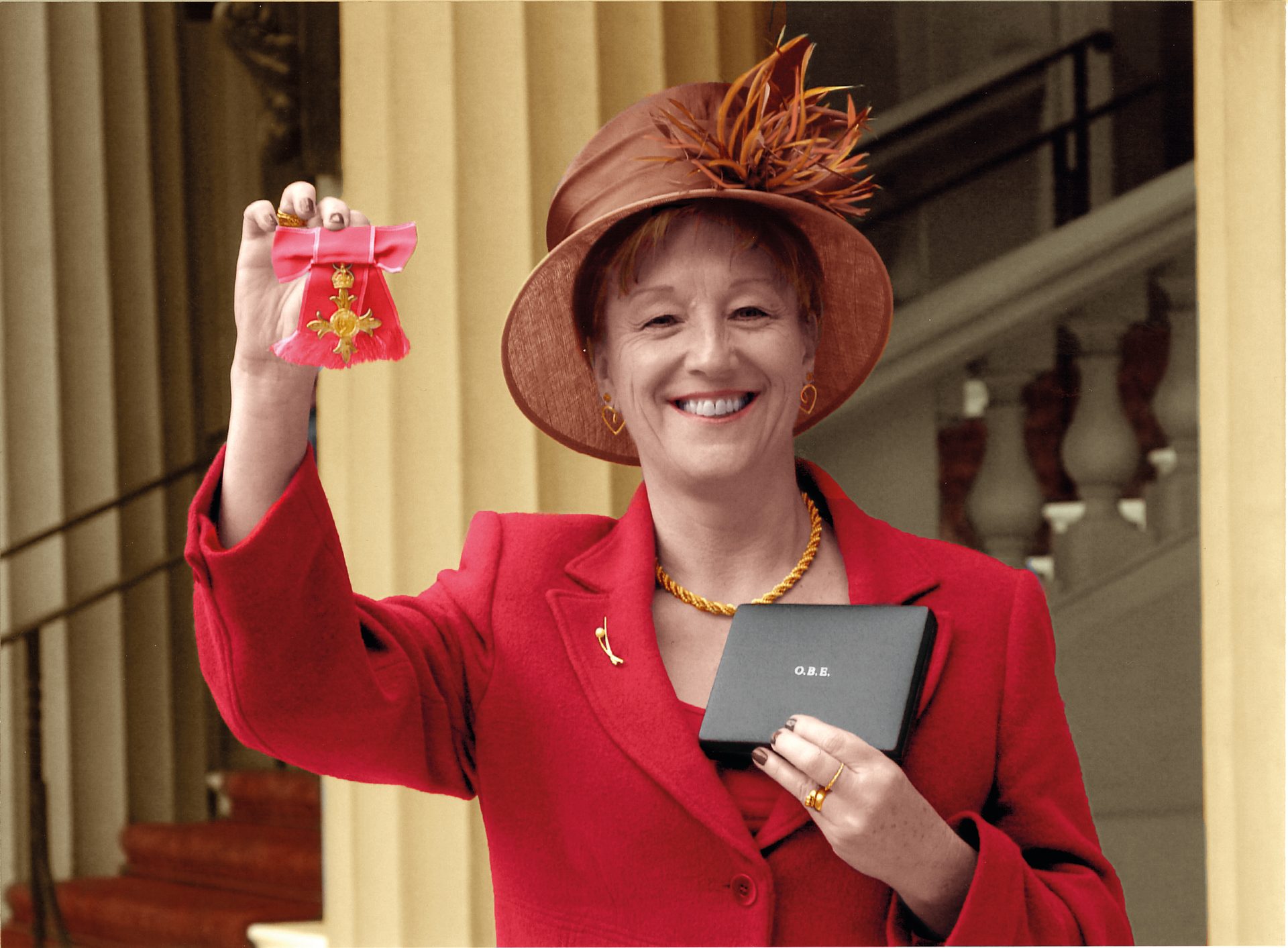 Smiling woman in red hat and suit holds up a GBE medal and box outside a grand building.