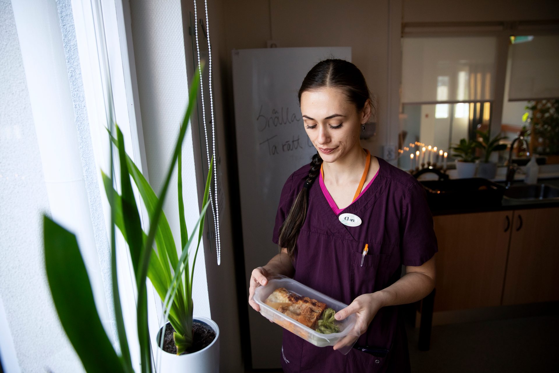 Clara in scrubs holds a meal prep container with food.