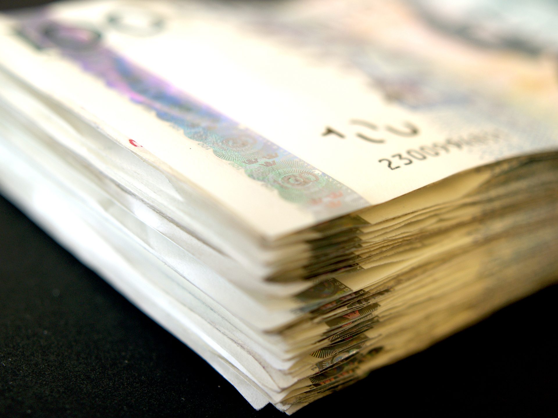 Close-up of a thick stack of currency banknotes, with focus on security features and serial numbers.