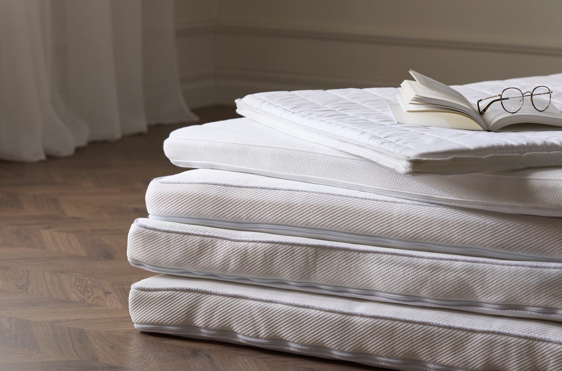 Stack of white mattress toppers on a wooden floor, with an open book and eyeglasses on top.
