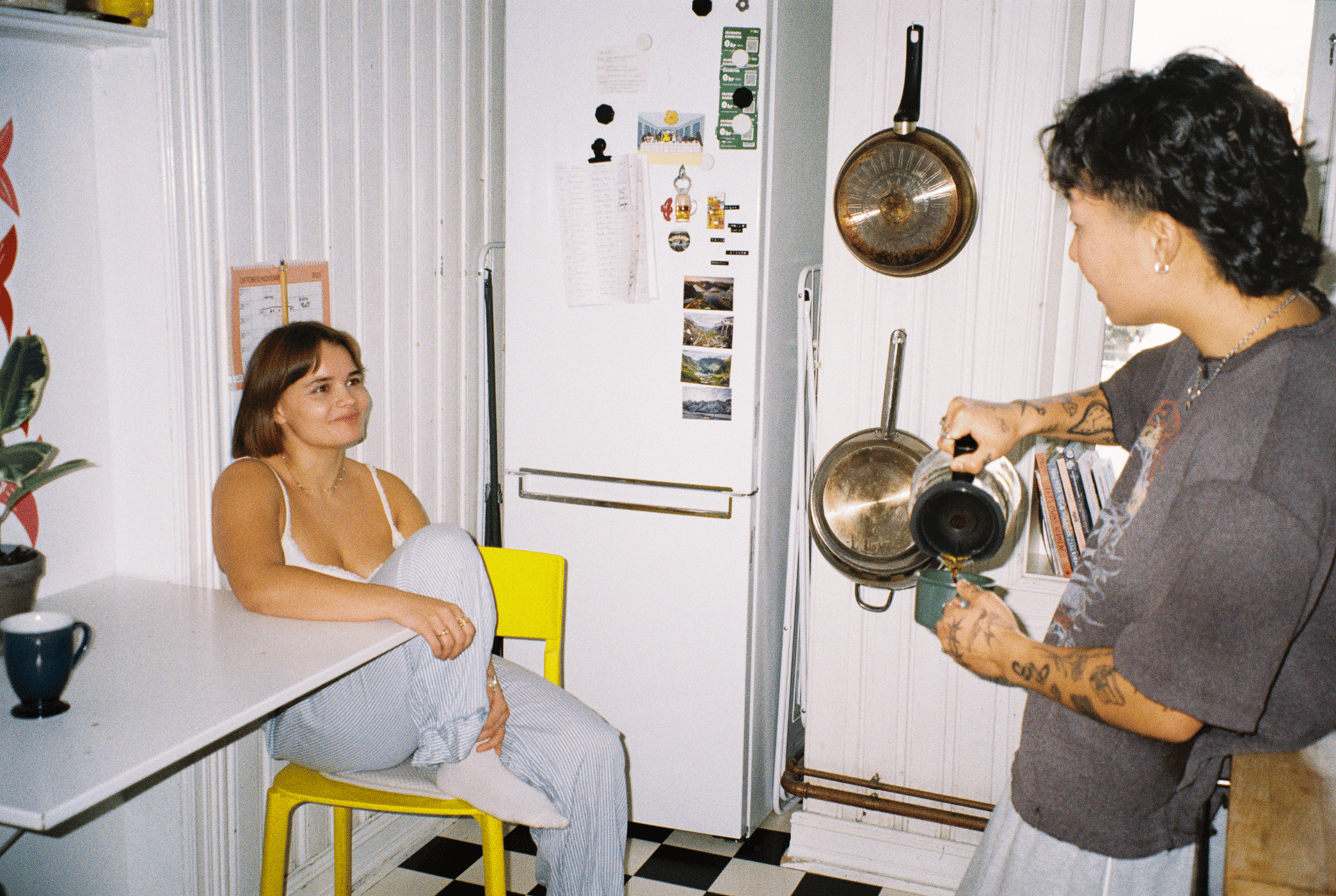 Two people in a kitchen, one pouring coffee for the other who is seated at a table.