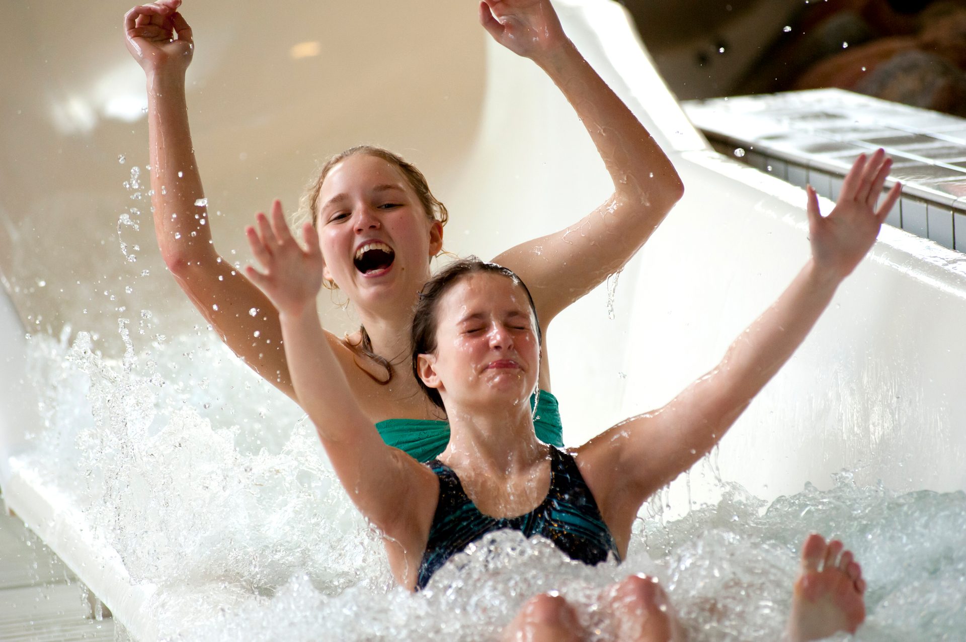 Joyful girls on a water slide, arms up, amidst a big splash.