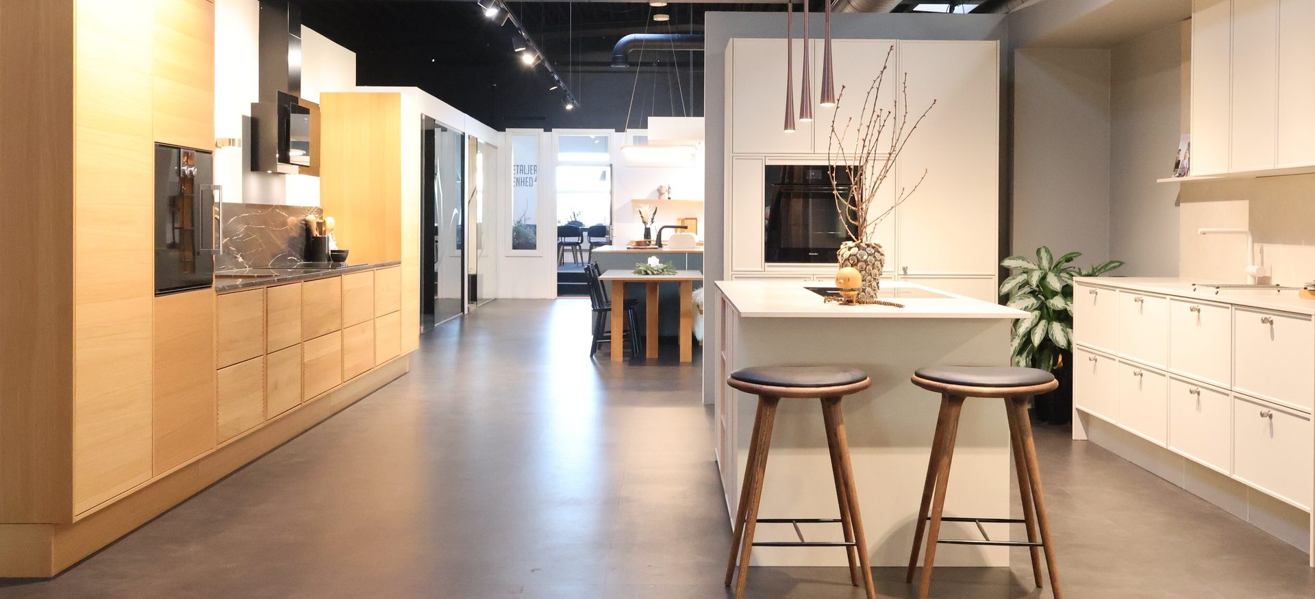 Modern kitchen showroom with light wood and white cabinetry, island, and dark flooring.