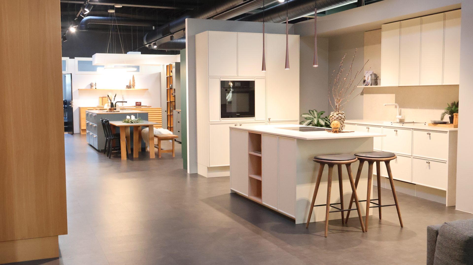 Modern kitchen showroom with light cream cabinets, islands, stools, and integrated appliances.