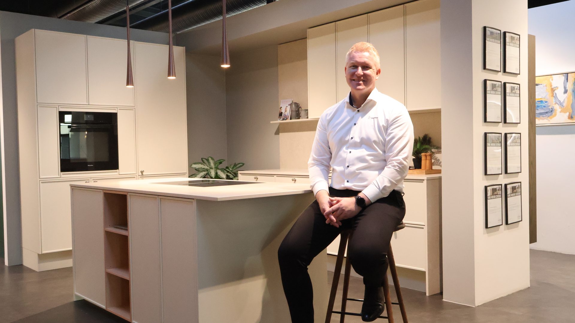 A man sits on a stool in a stylish, light-colored kitchen showroom.