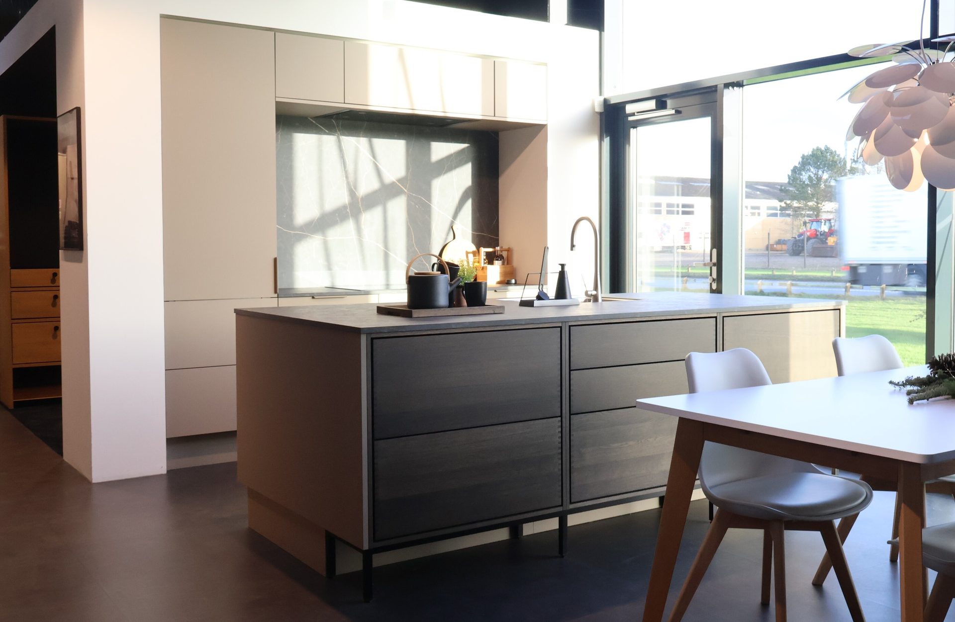 Bright modern kitchen with island, dining area, light cabinets, and large windows.