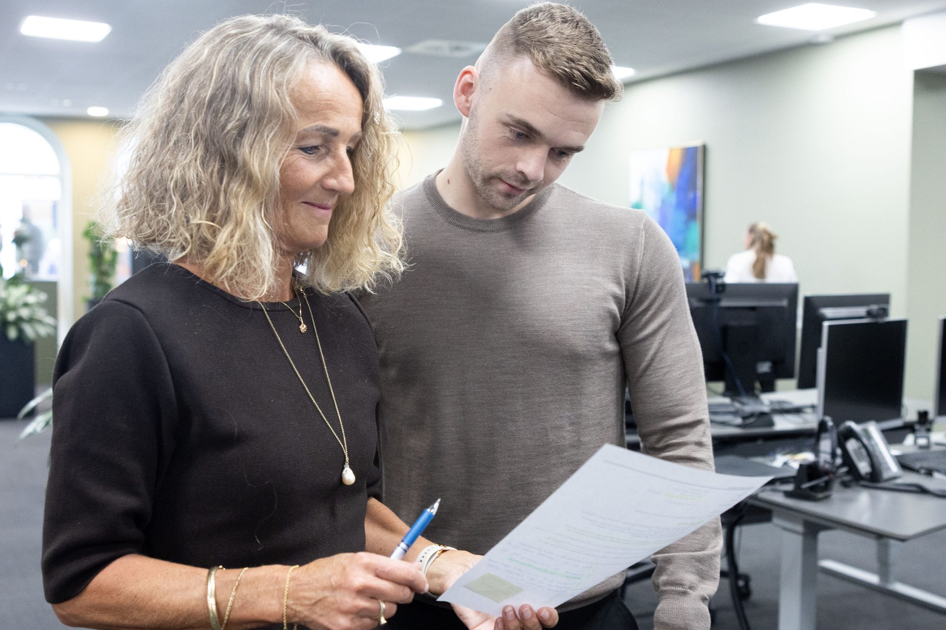 An older woman and a younger man review a document together in an office.