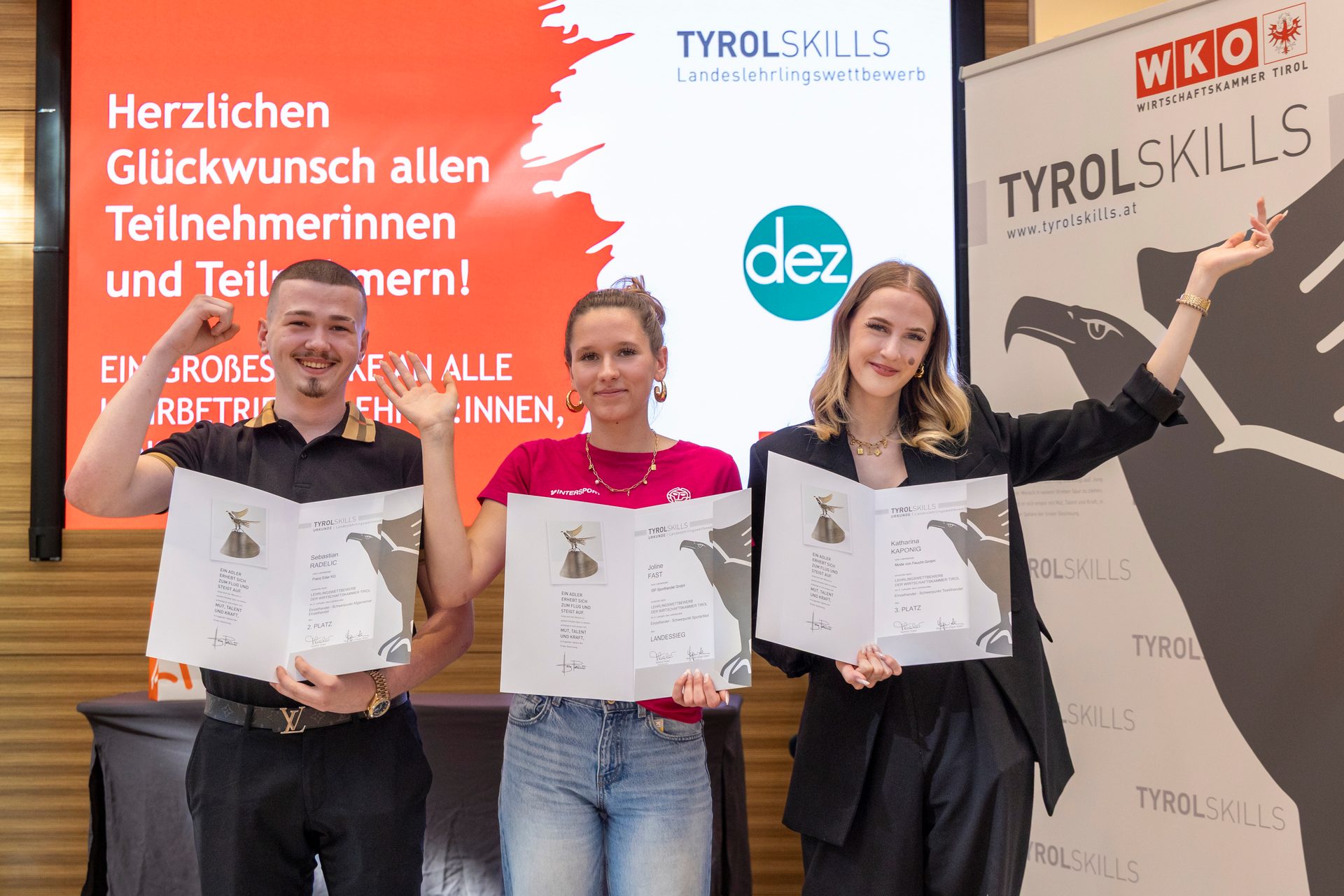Three smiling participants hold certificates at the TyrolSkills competition award ceremony.