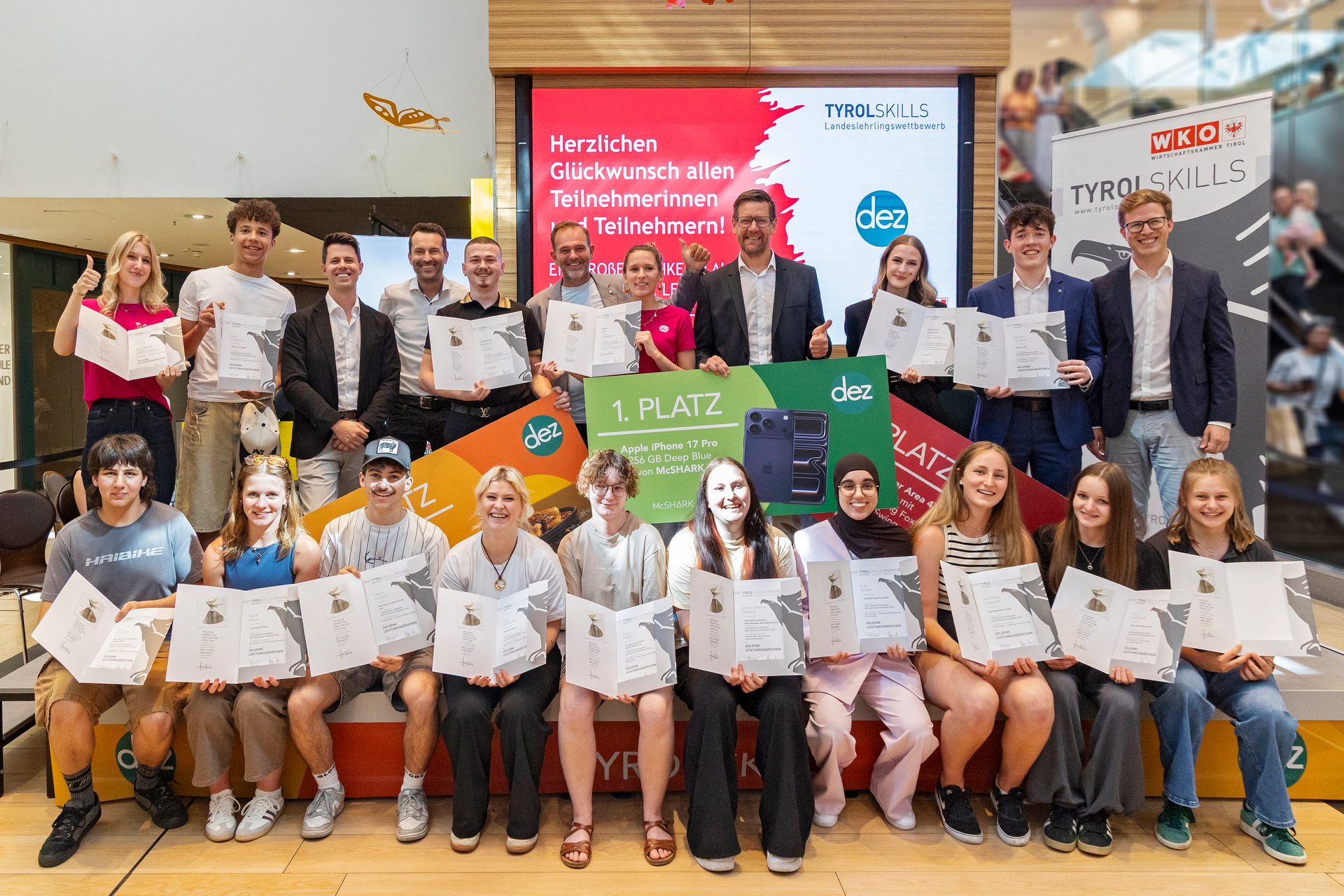 A diverse group of young people and adults smiling and holding certificates at an awards ceremony under a 'TYROLSKILLS' banner.