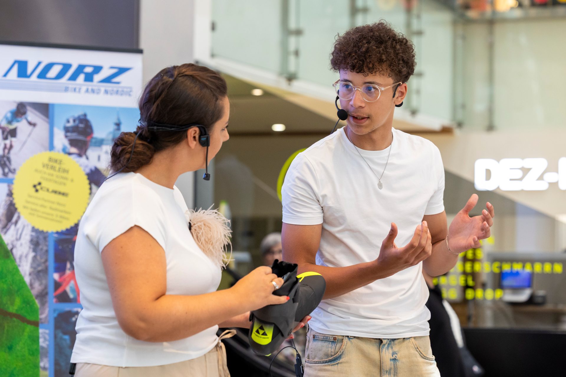 Two people with headsets discuss a black and yellow shoe in a retail setting.