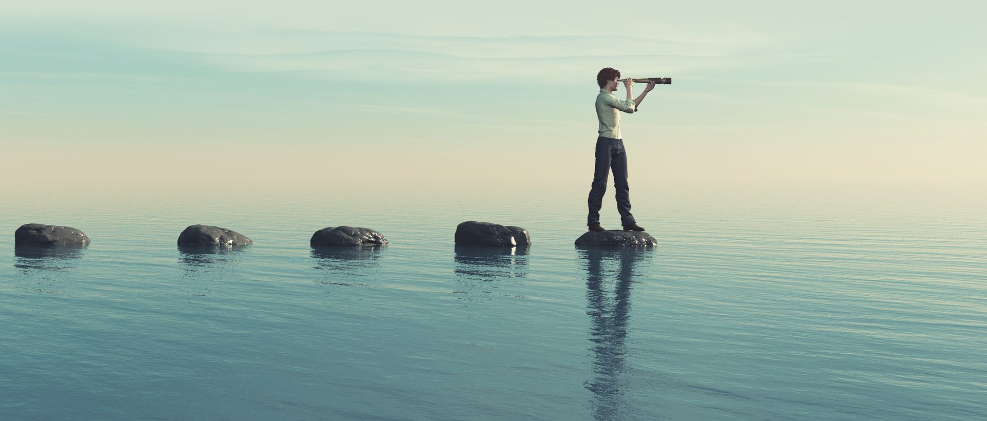 Young man on a large stone in the middle of the sea looking through binoculars