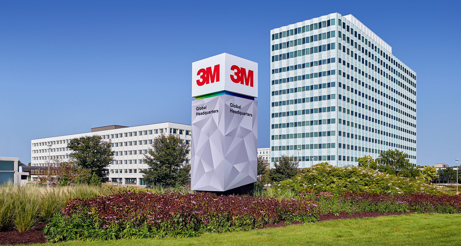 3M Global Headquarters campus with its prominent sign, a tall white office building, and lush green landscaping.