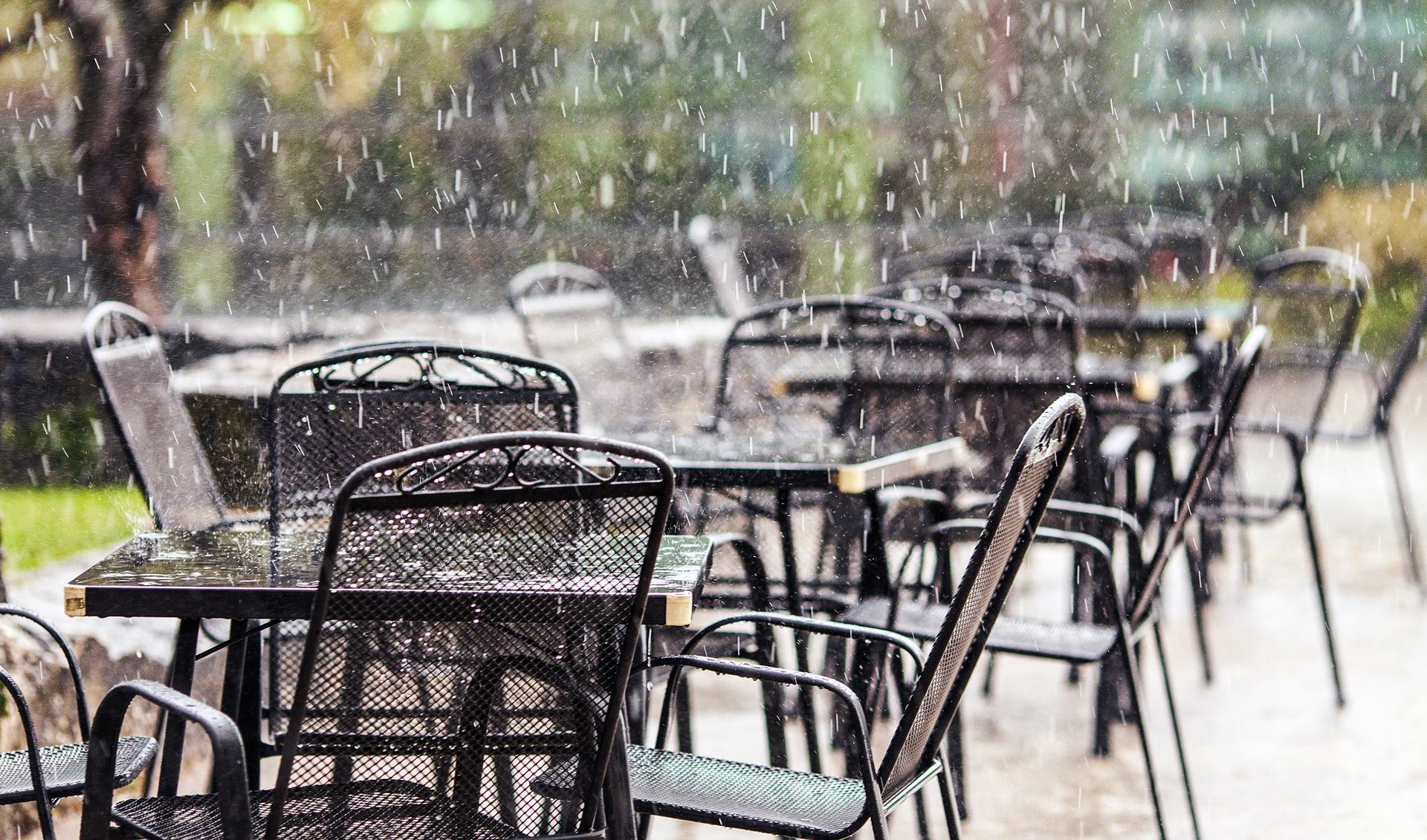 Empty metal outdoor cafe tables and chairs in heavy rain.