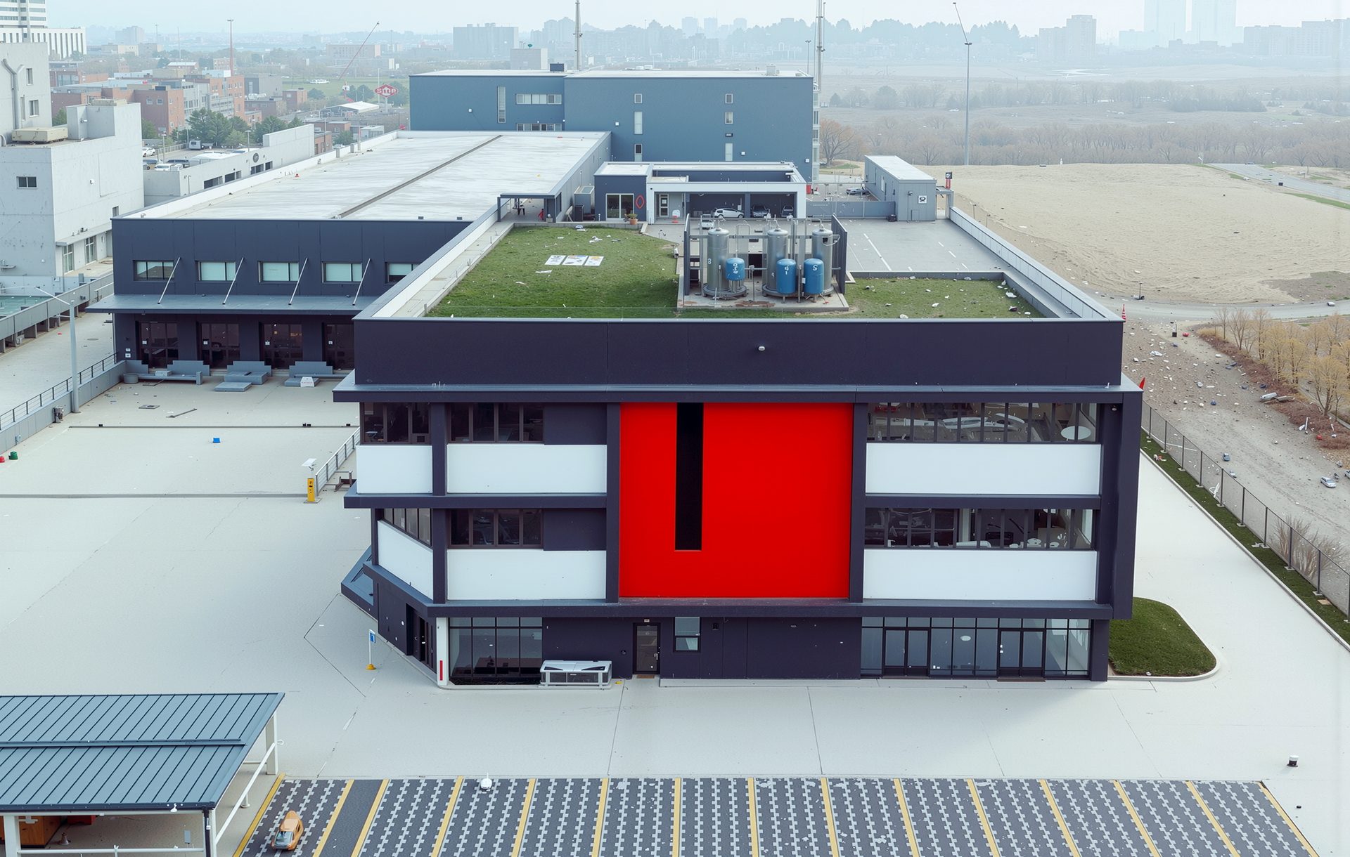 Modern building with dark grey and white facade, red accent, green roof, and large paved area.