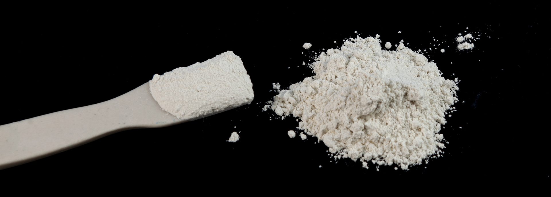 Pile of White Chemical Powder on black table, selective focus. Laboratory Spatula with Titanium dioxide powder, TiO2.