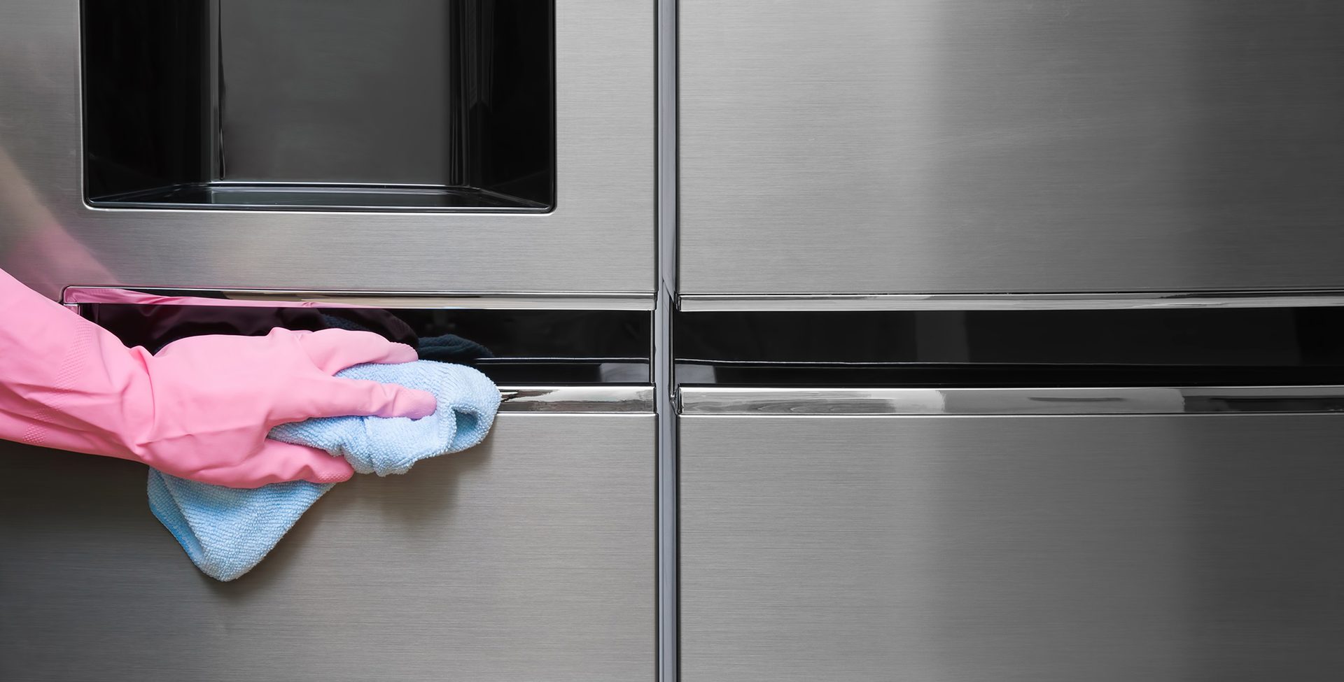 Employee hand in rubber protective glove with micro fiber cloth wiping a fridge's stainless doors.