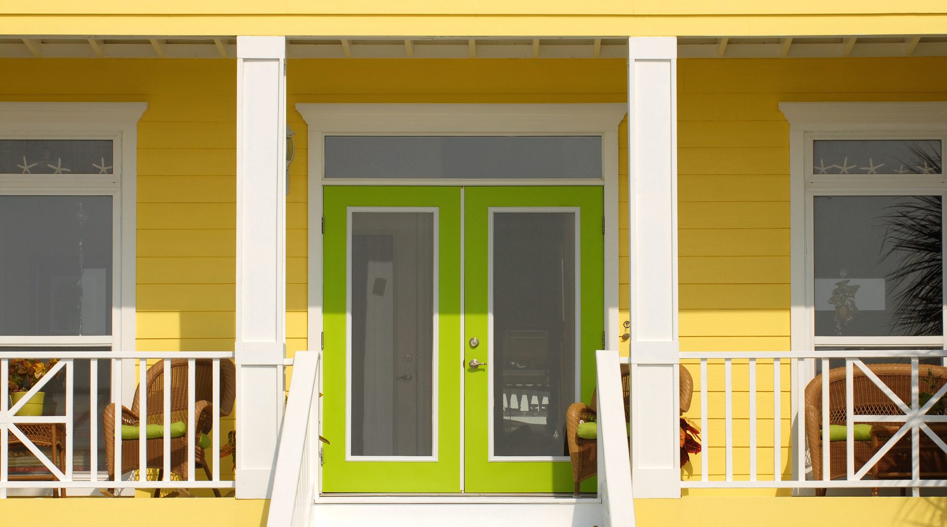 A vibrant lime green double door entrance on a bright yellow house with a white porch and railings.