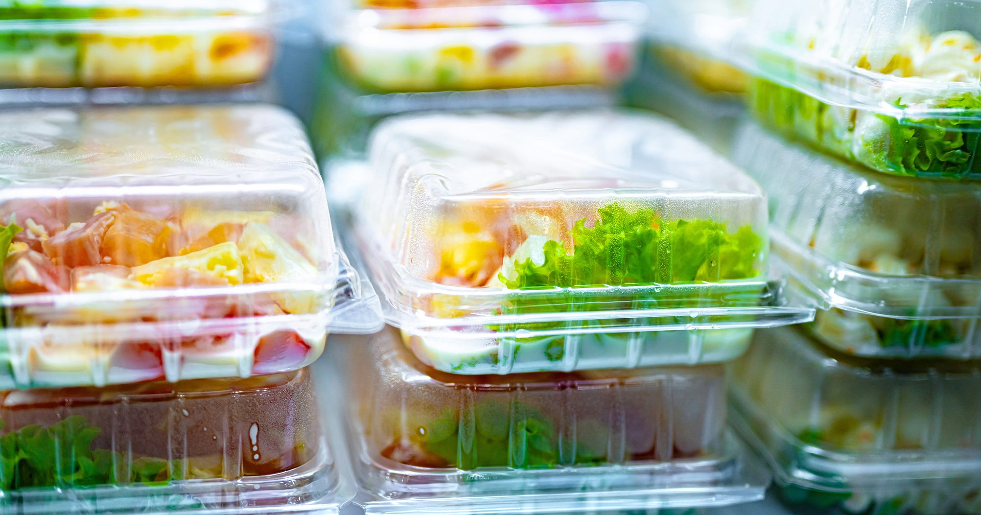 Stacked plastic containers filled with fresh salads and meal prep items, ready for take-away or retail.