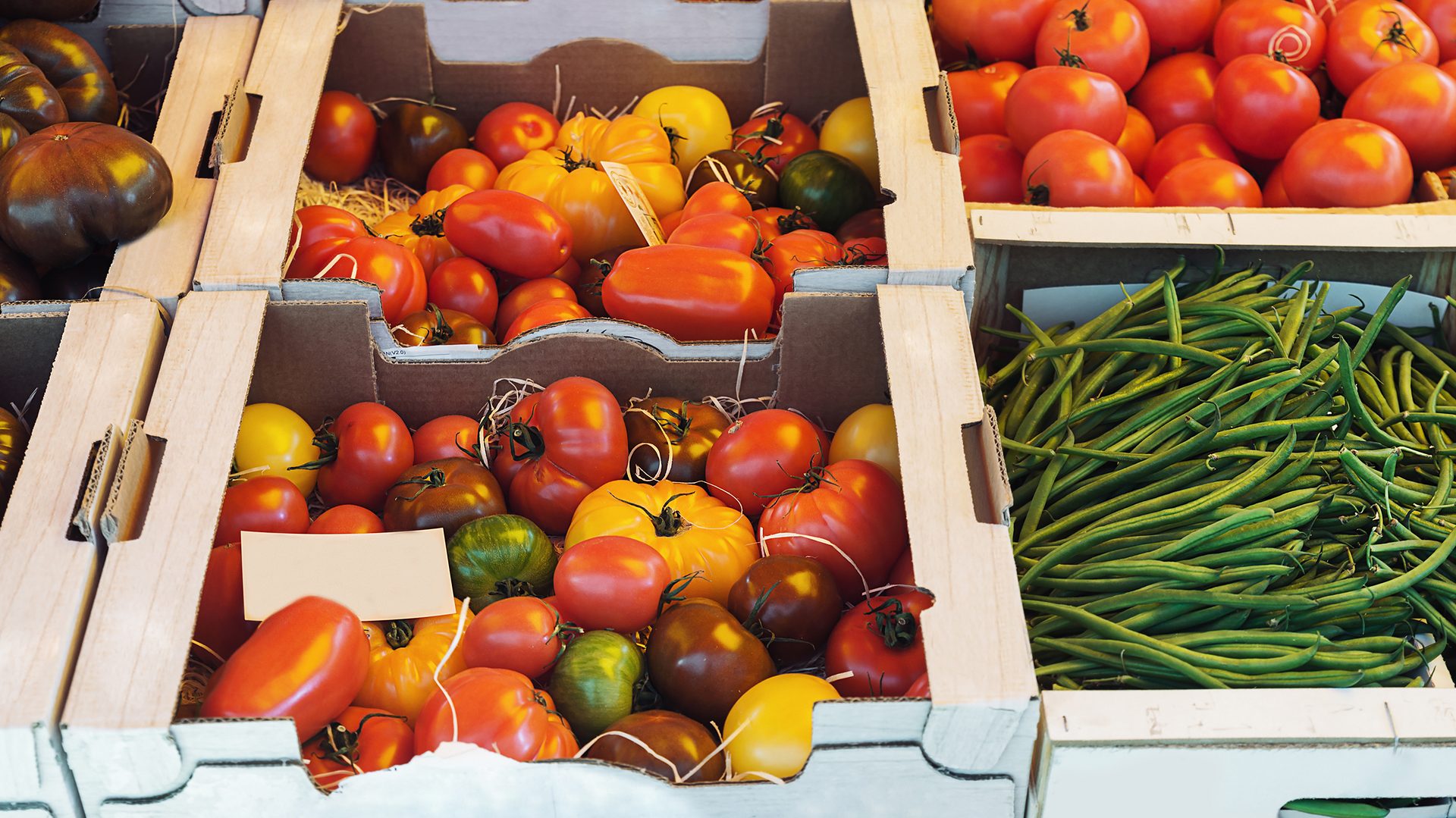 Open air market stand selling peppers, tomatoes and green beans in crates