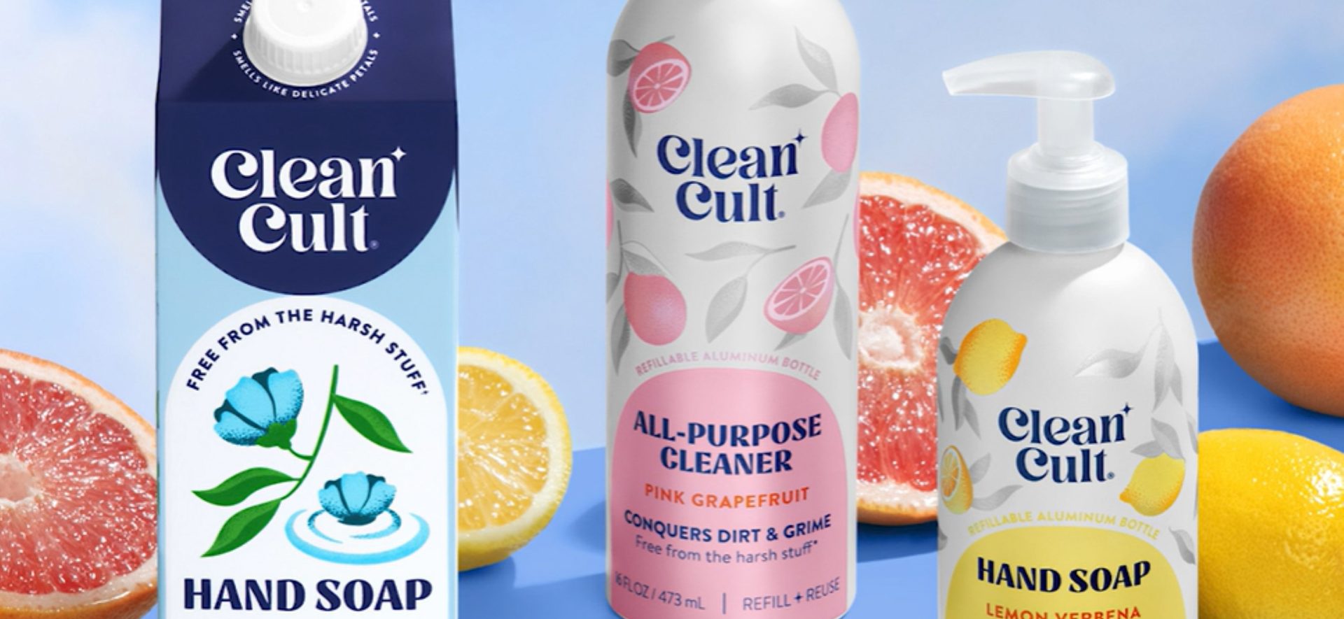 Three Clean Cult products: a hand soap refill carton, a pink grapefruit all-purpose cleaner, and a lemon verbena hand soap bottle, surrounded by halved grapefruits and lemons.