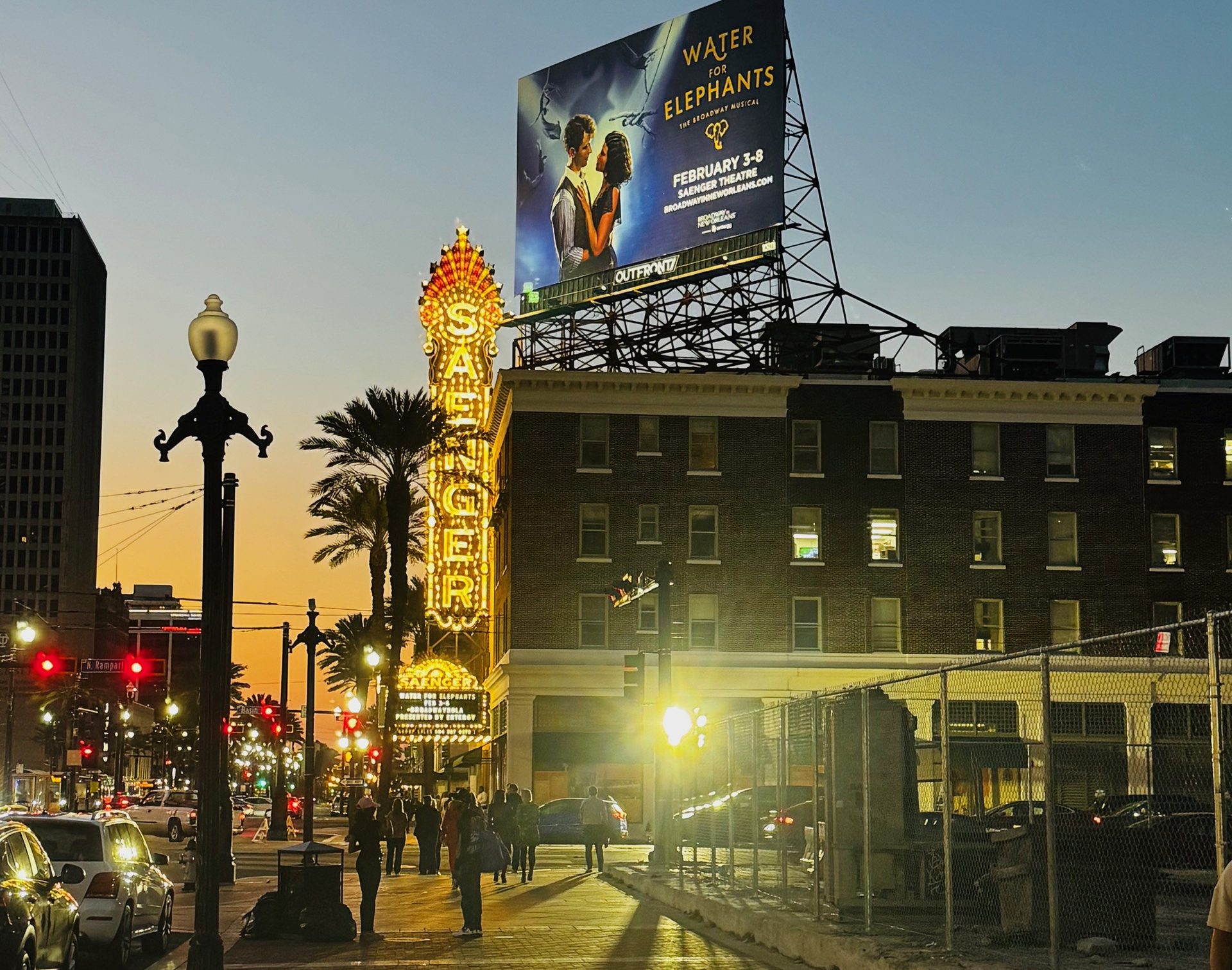Neon Saenger sign and "Water for Elephants" billboard illuminate a vibrant street scene at dusk.