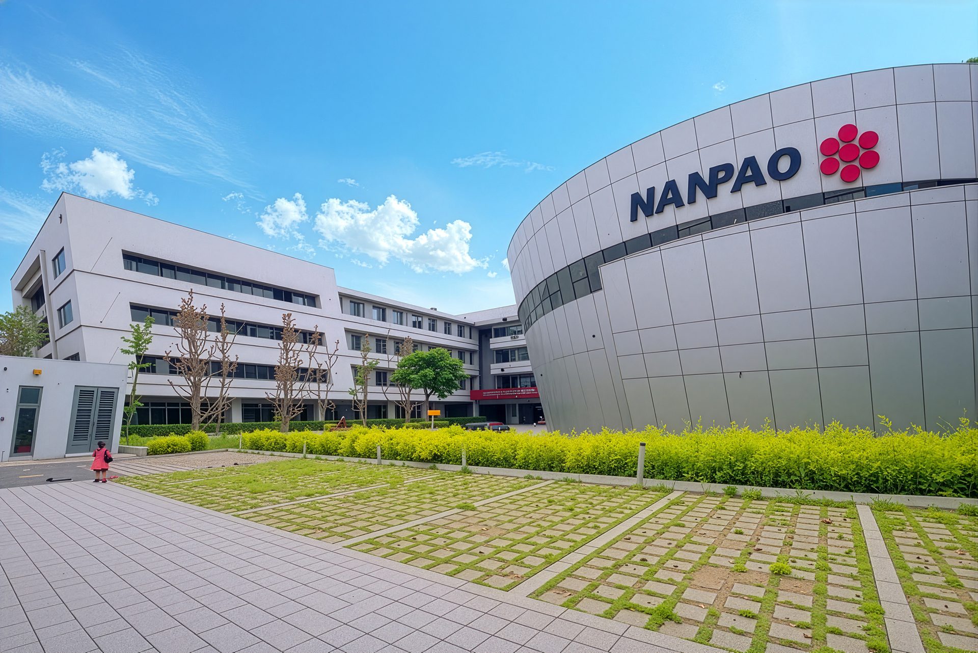 Modern corporate campus featuring the curved NANPAO building, green landscaping, and parking grid under a blue sky.