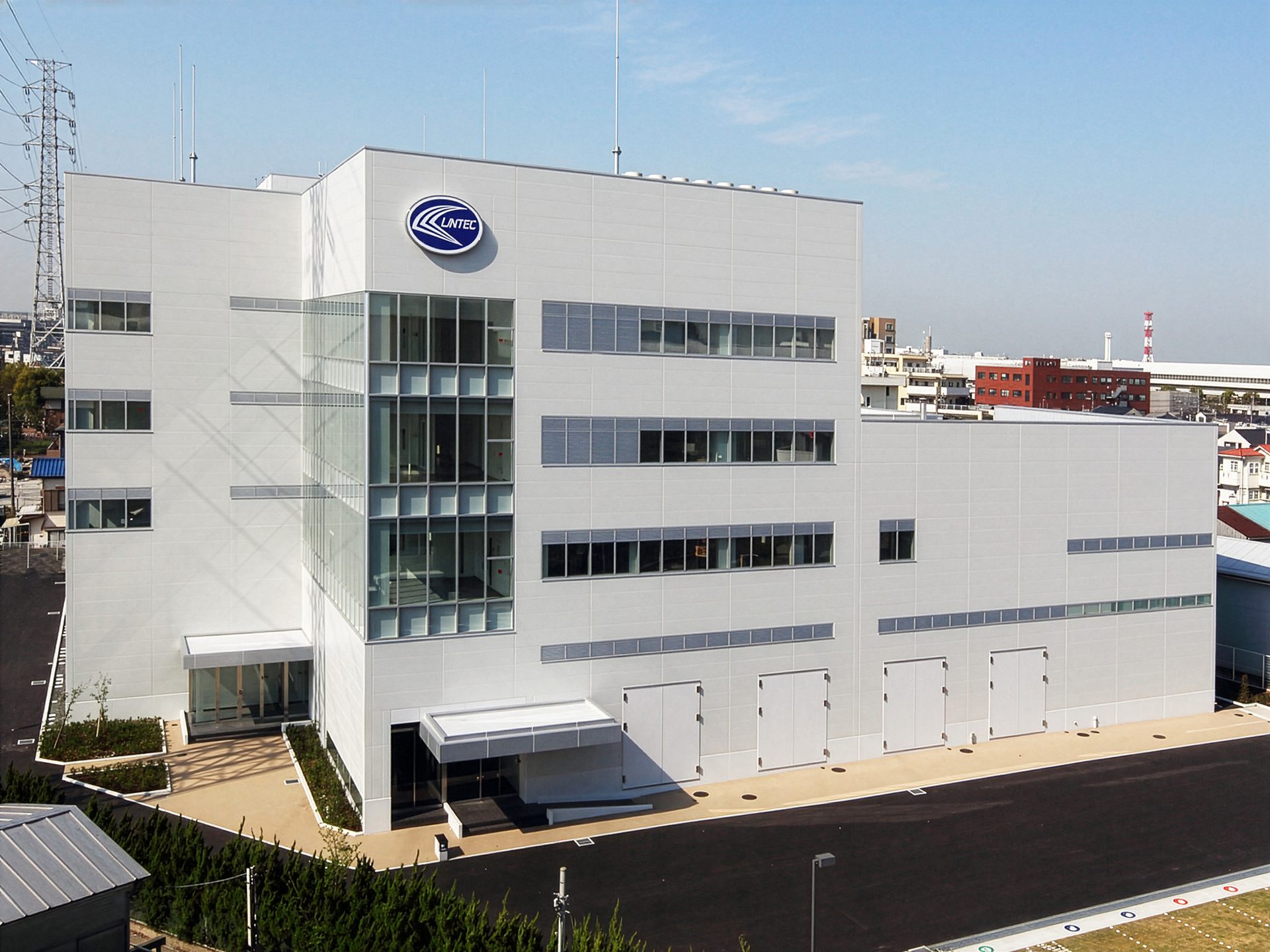 A modern white building with a blue "LINTEC" logo, large glass facades, and multiple ground-level entrances.