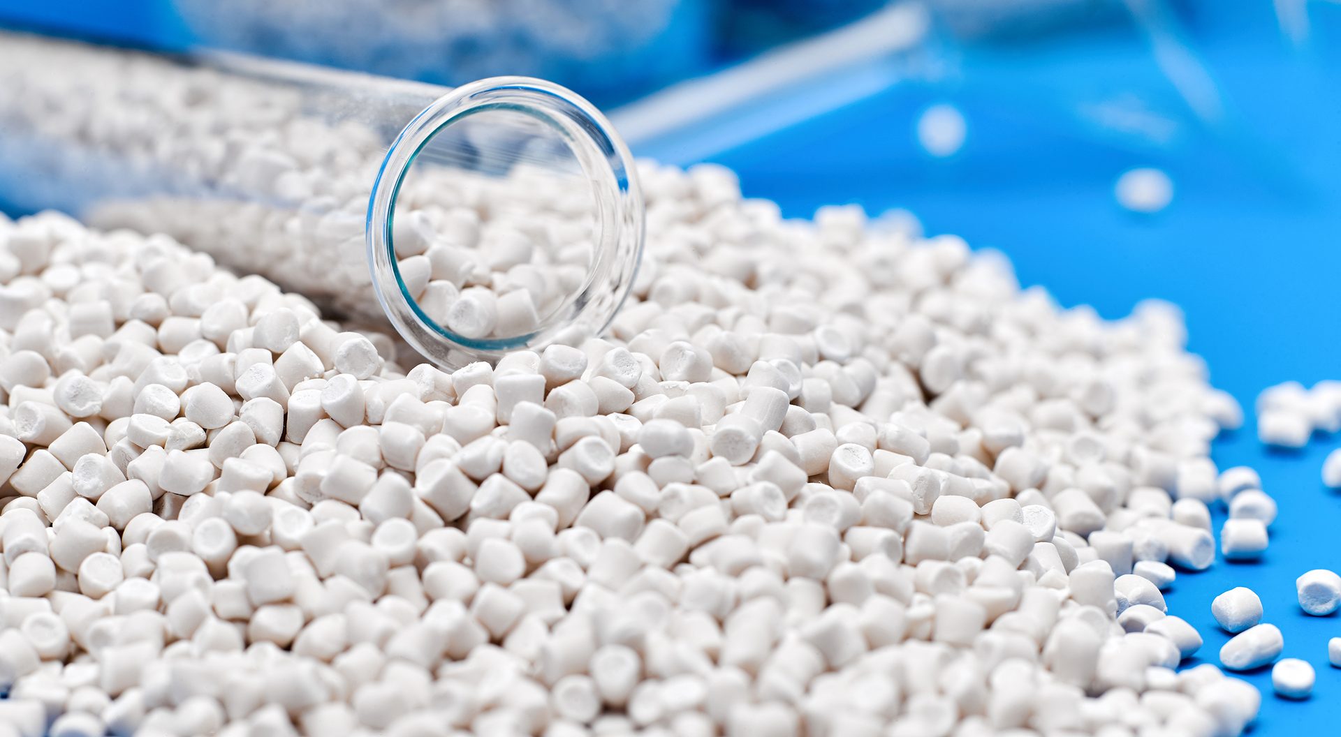 Closeup of a white polymer granule with a chemical flask on a bright blue background.