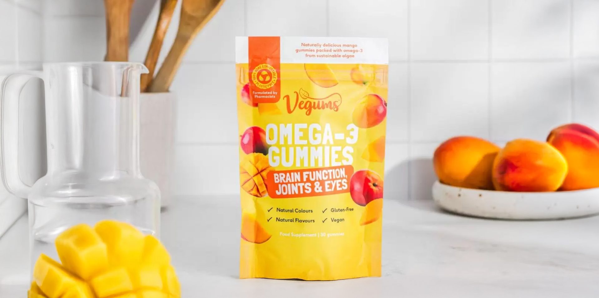 Pouch of Vegums Gummies on kitchen counter with wooden spoons and bowl of fruit behind it