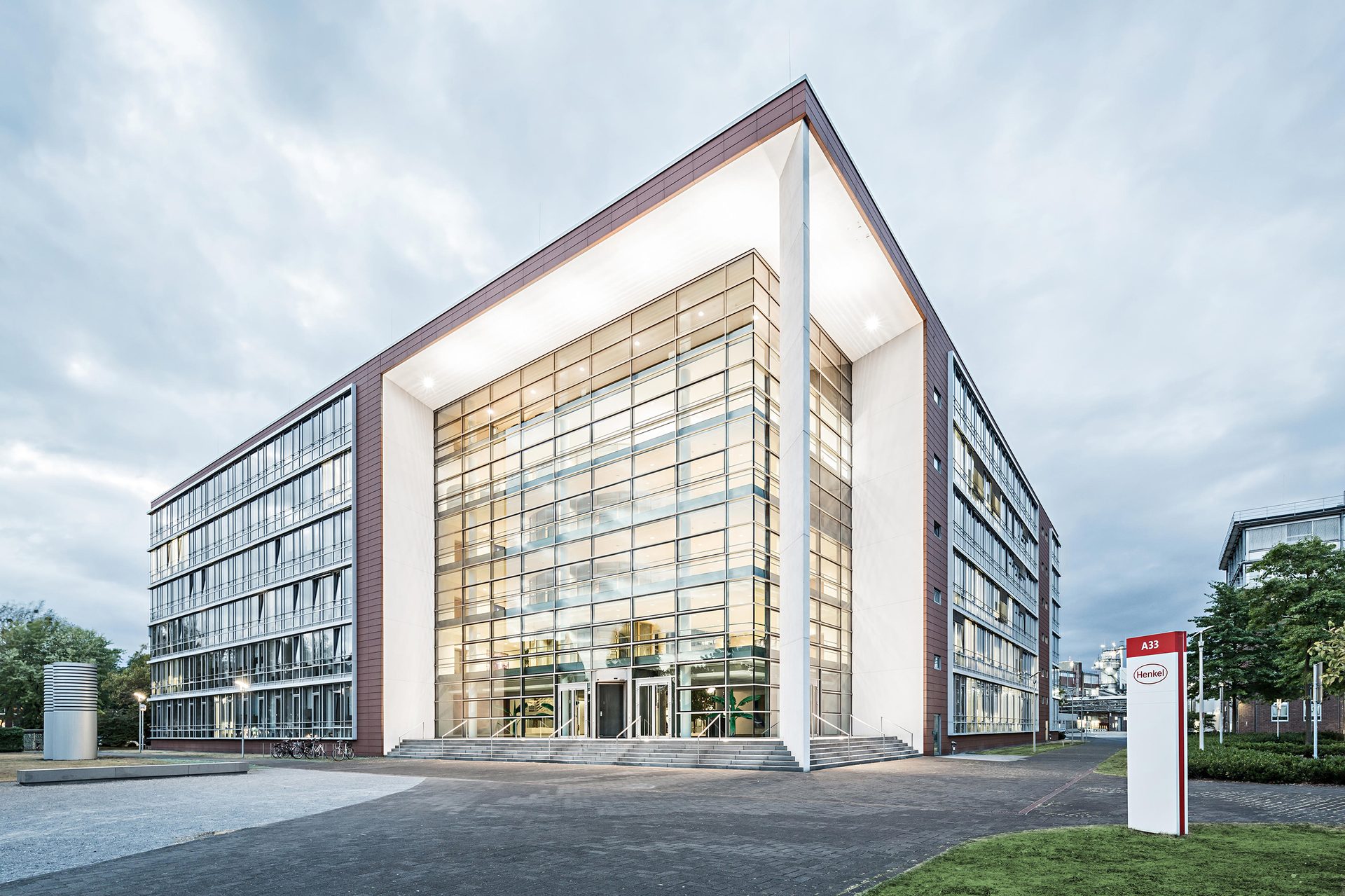 A modern office building featuring a large glass facade entrance, surrounded by pathways and green areas.