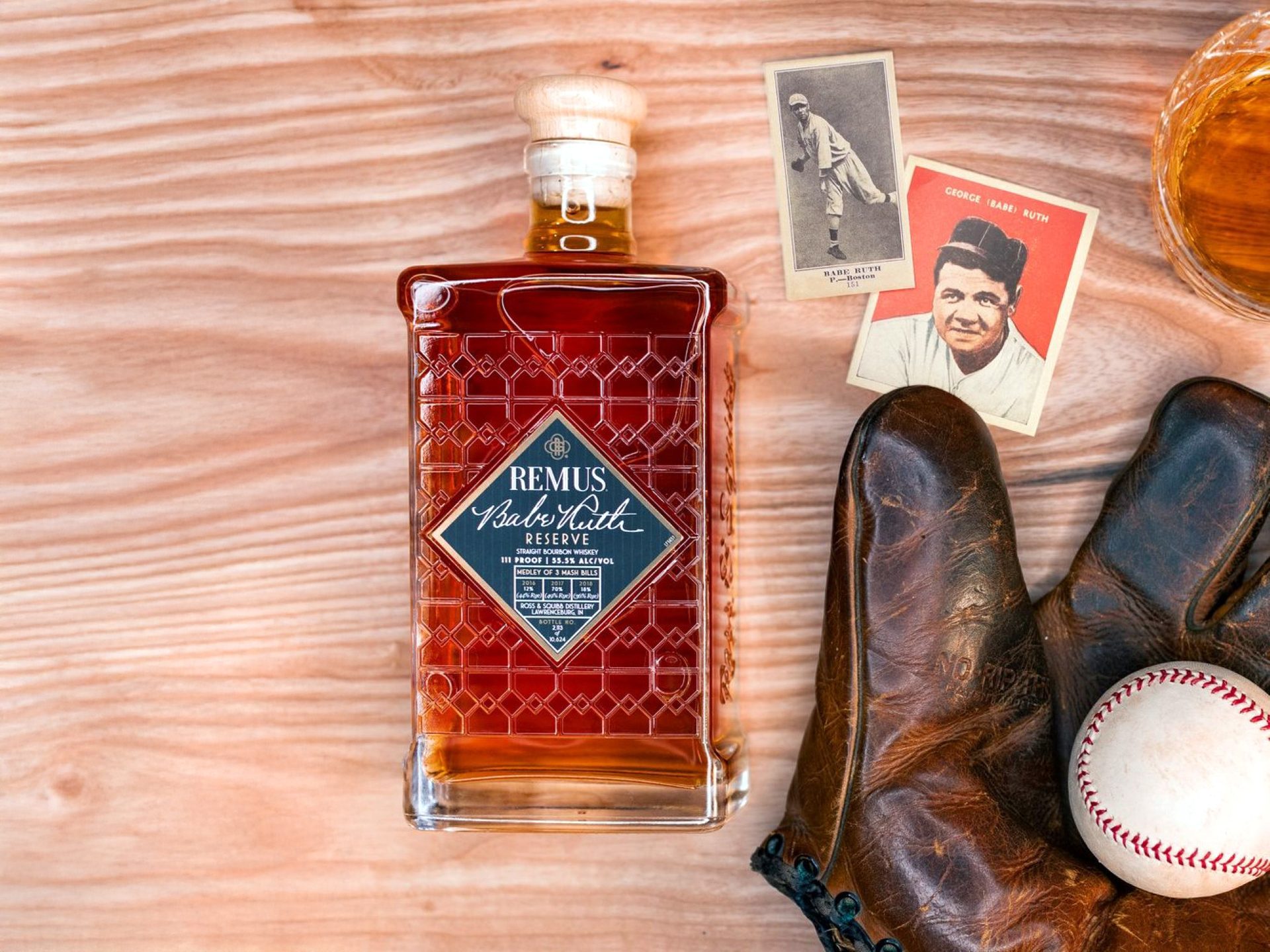 Remus bottle laying flat next to a baseball in a glove with Babe Ruth memorabilia.