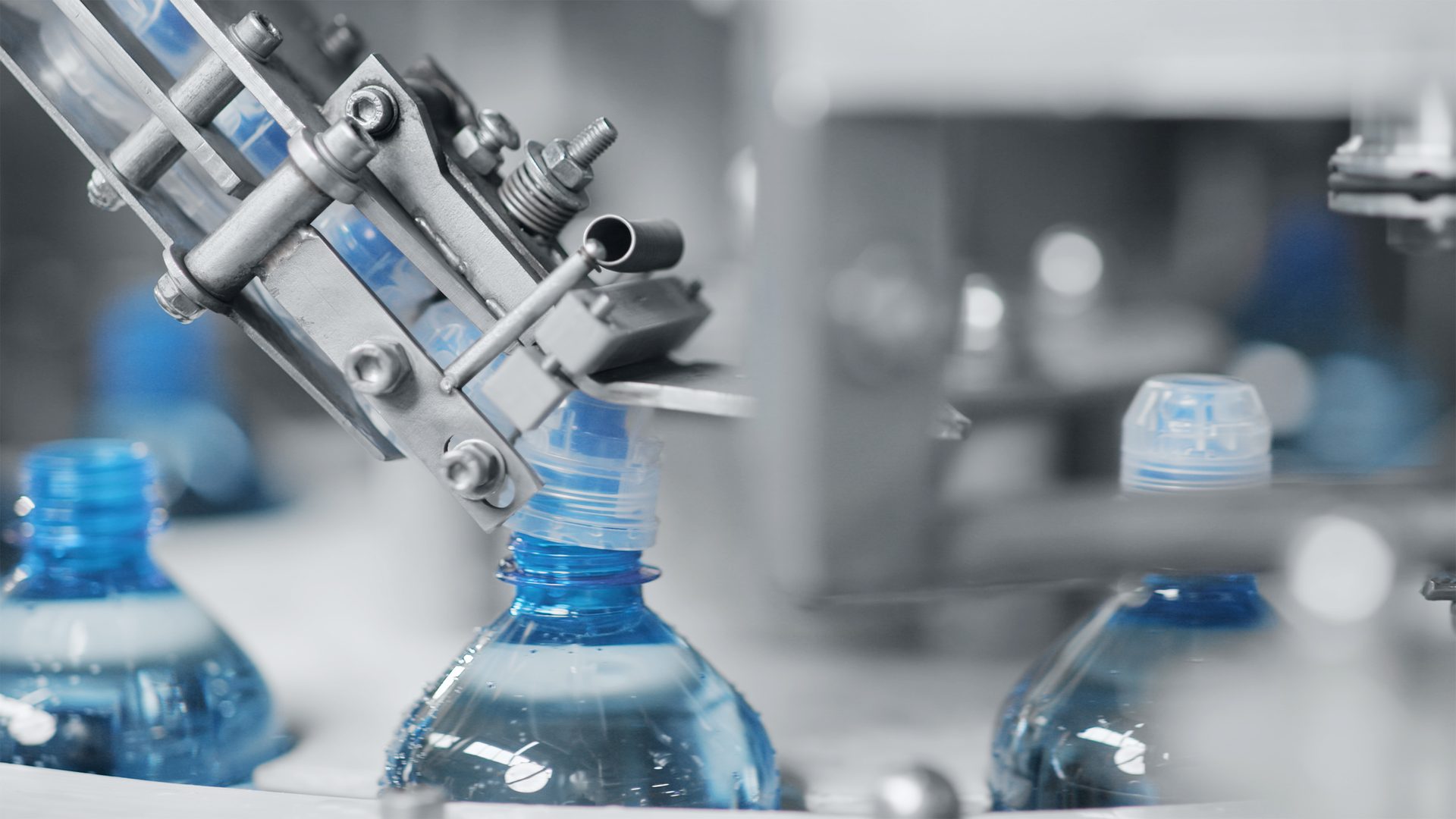 Machinery putting caps on blue water bottles