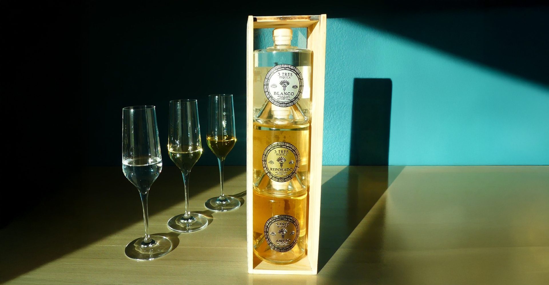 Three 3 Tres bottles stacked on top of each other in wooden packaging frame, with three glasses next to them.
