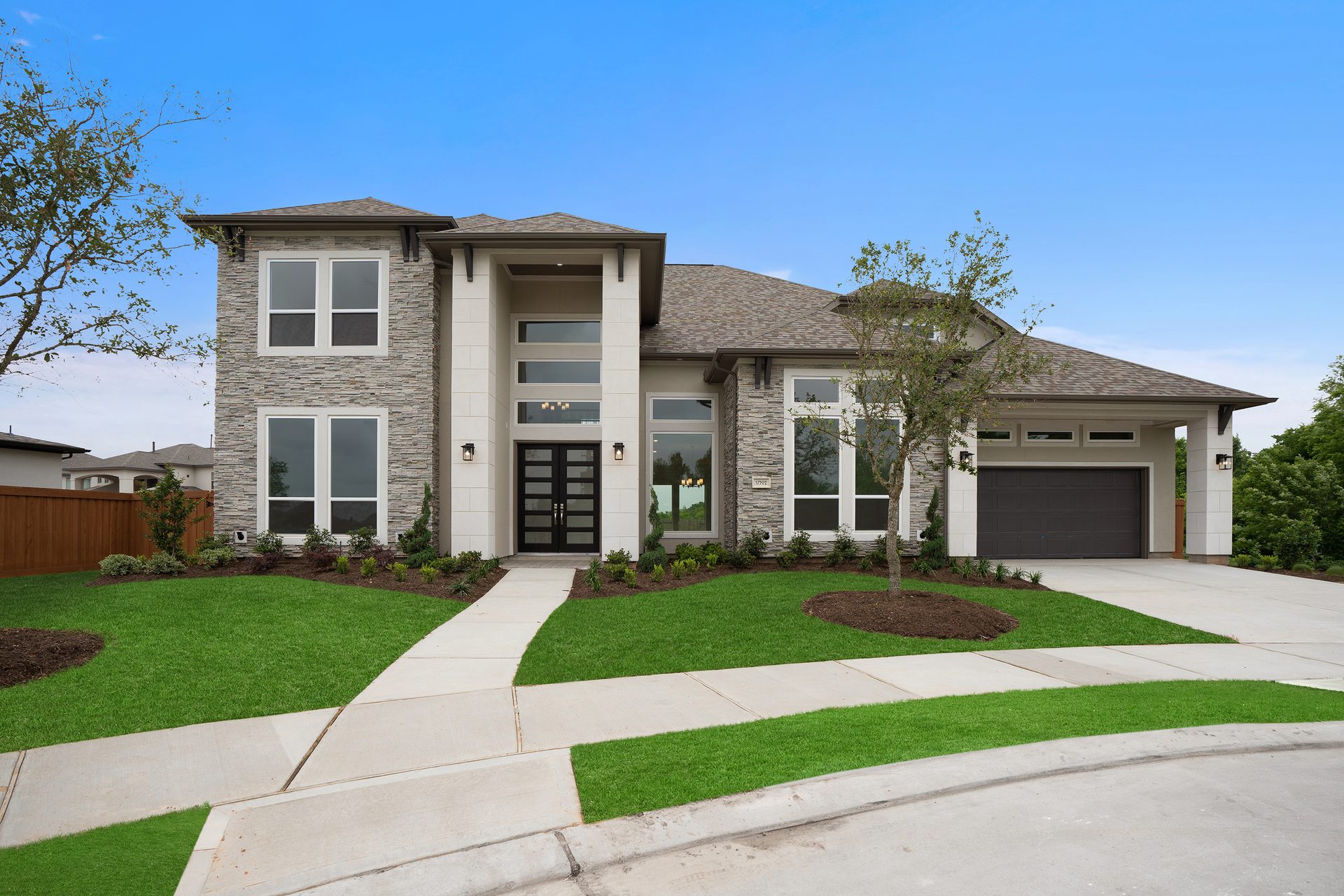 Modern gray stone and white stucco house with a dark roof, large windows, and a green lawn.