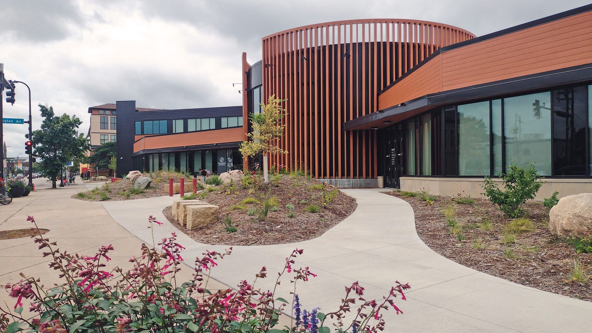 Modern building with a curved wooden facade, landscaped planters, and a winding path.
