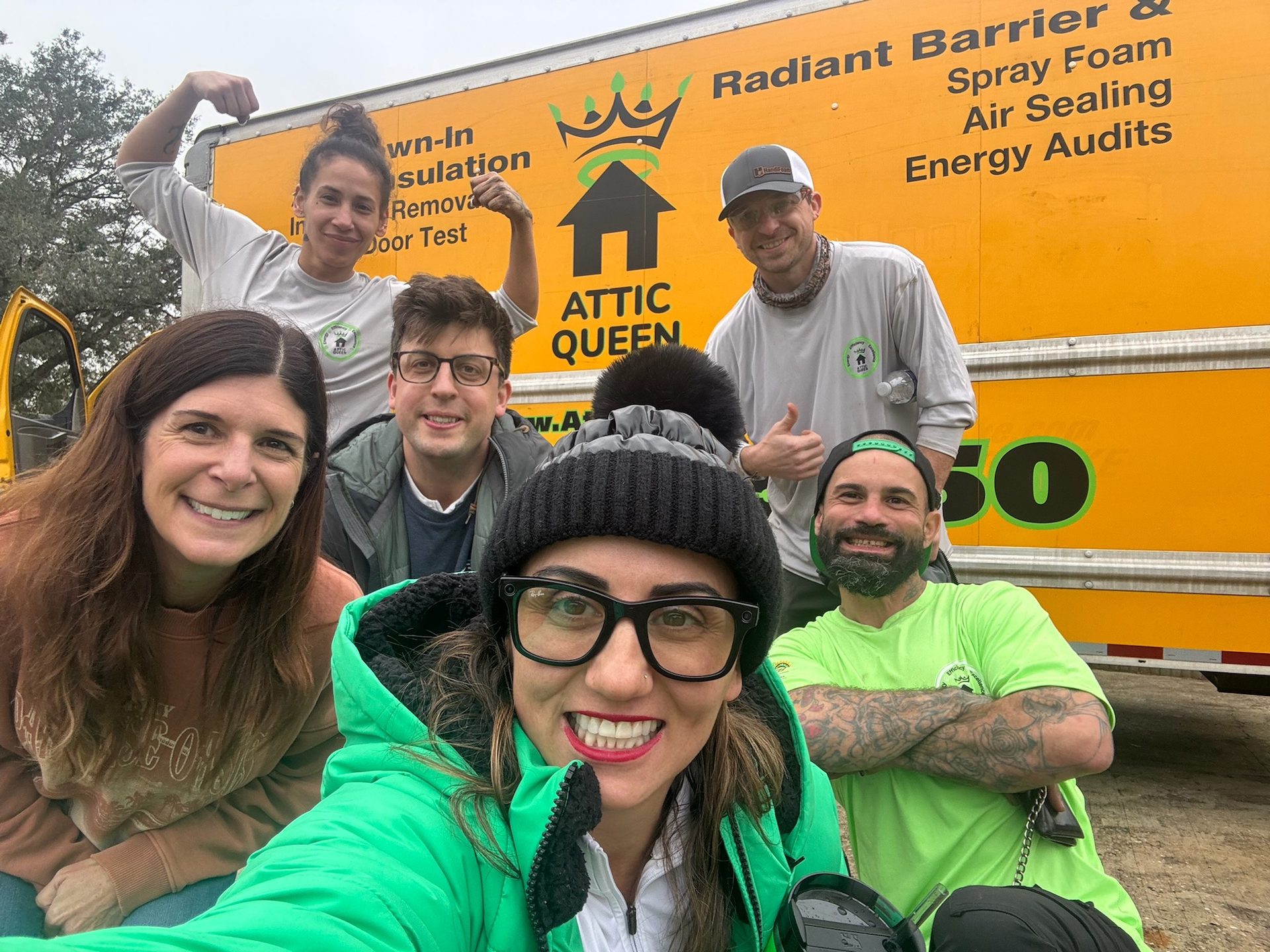 Six smiling people by an "Attic Queen" truck with attic insulation & energy audit services listed.