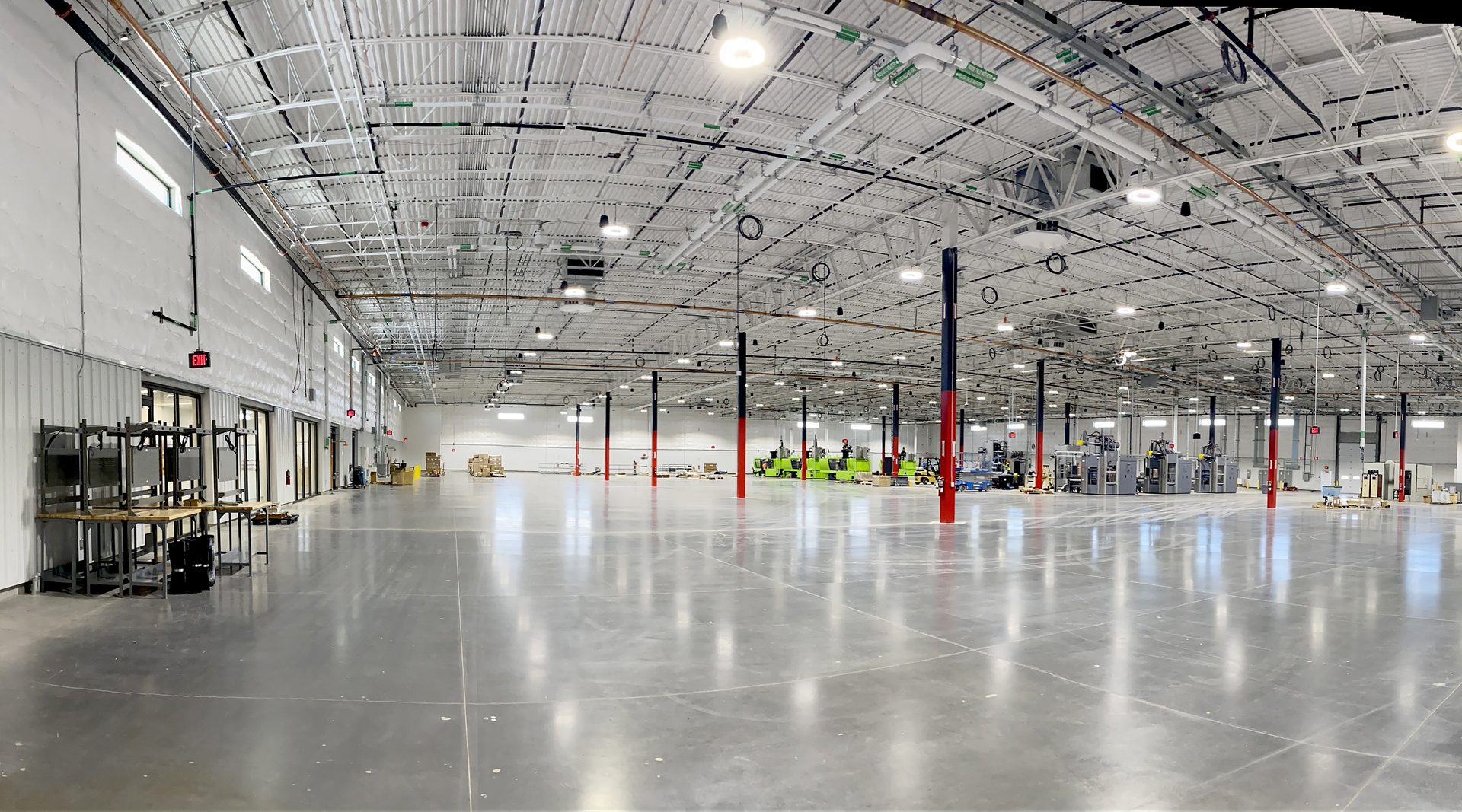 Spacious industrial interior with high ceilings, polished floor, red/black pillars, and machinery.
