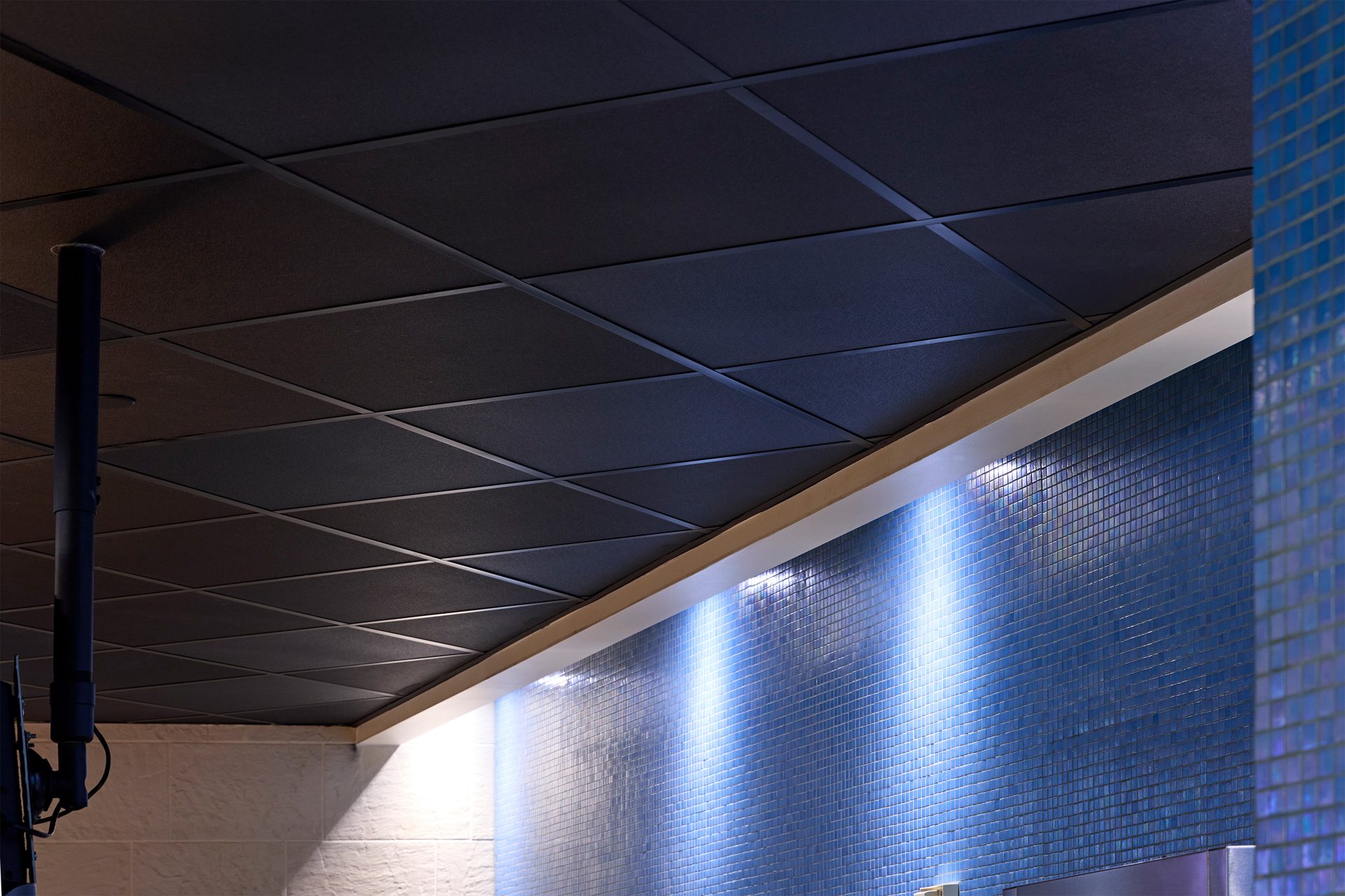 Dark grid ceiling above a blue tiled wall with uplighting.
